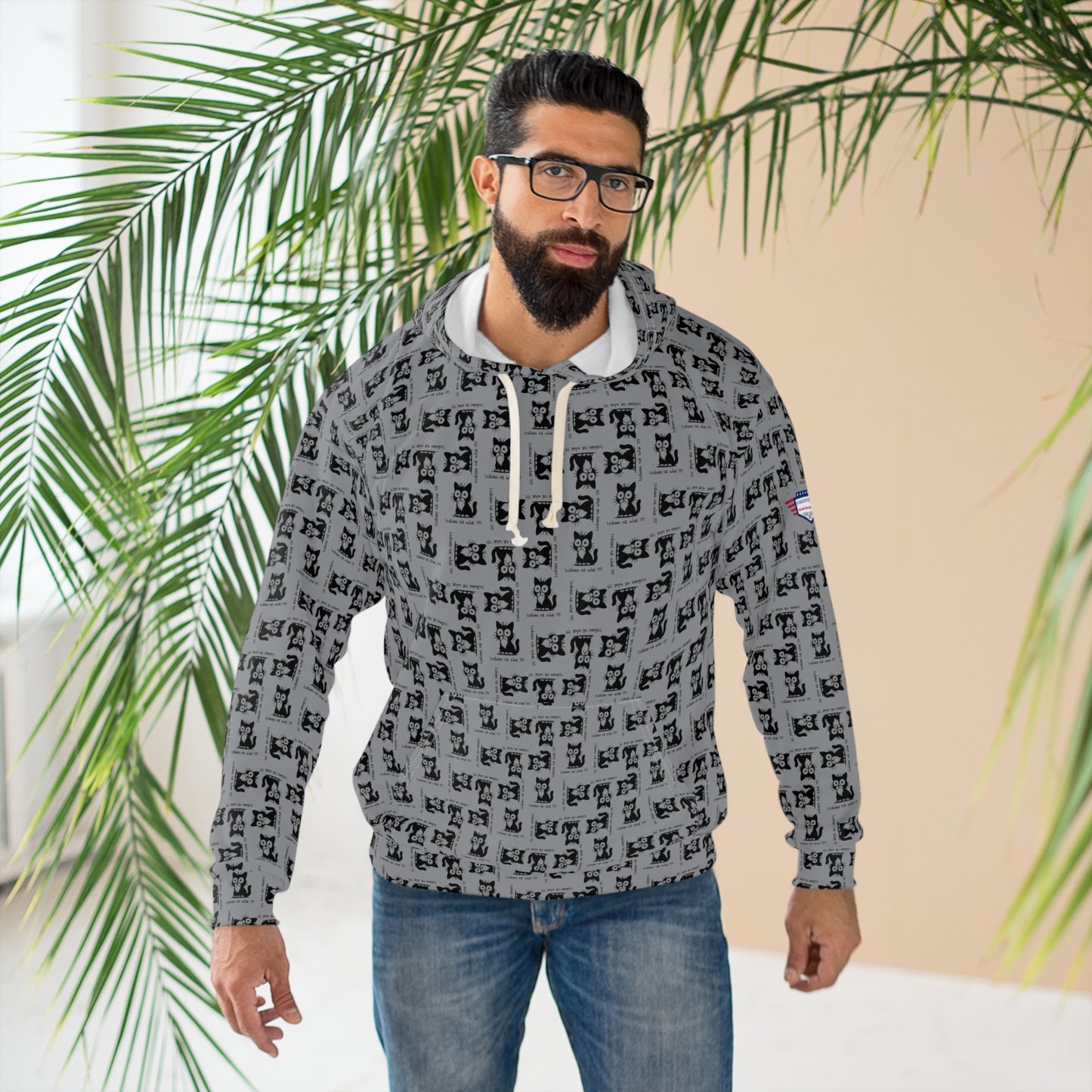 Bearded man in glasses rocking front view grey hoodie with tiled black vintage cats, palm backdrop