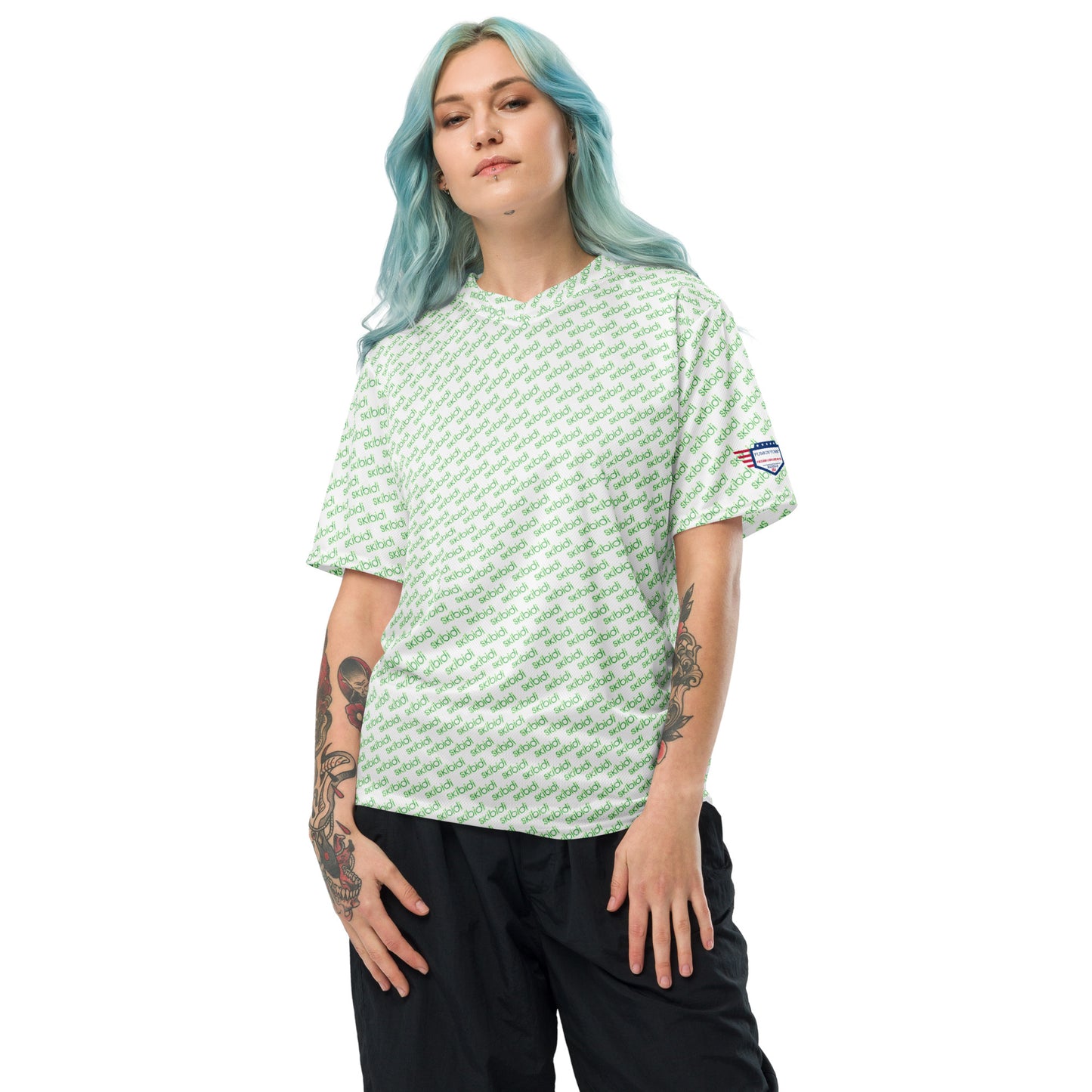 Blue-haired model flexing tattoo arm in white green "skibidi" all-over unisex sports jersey, black pants