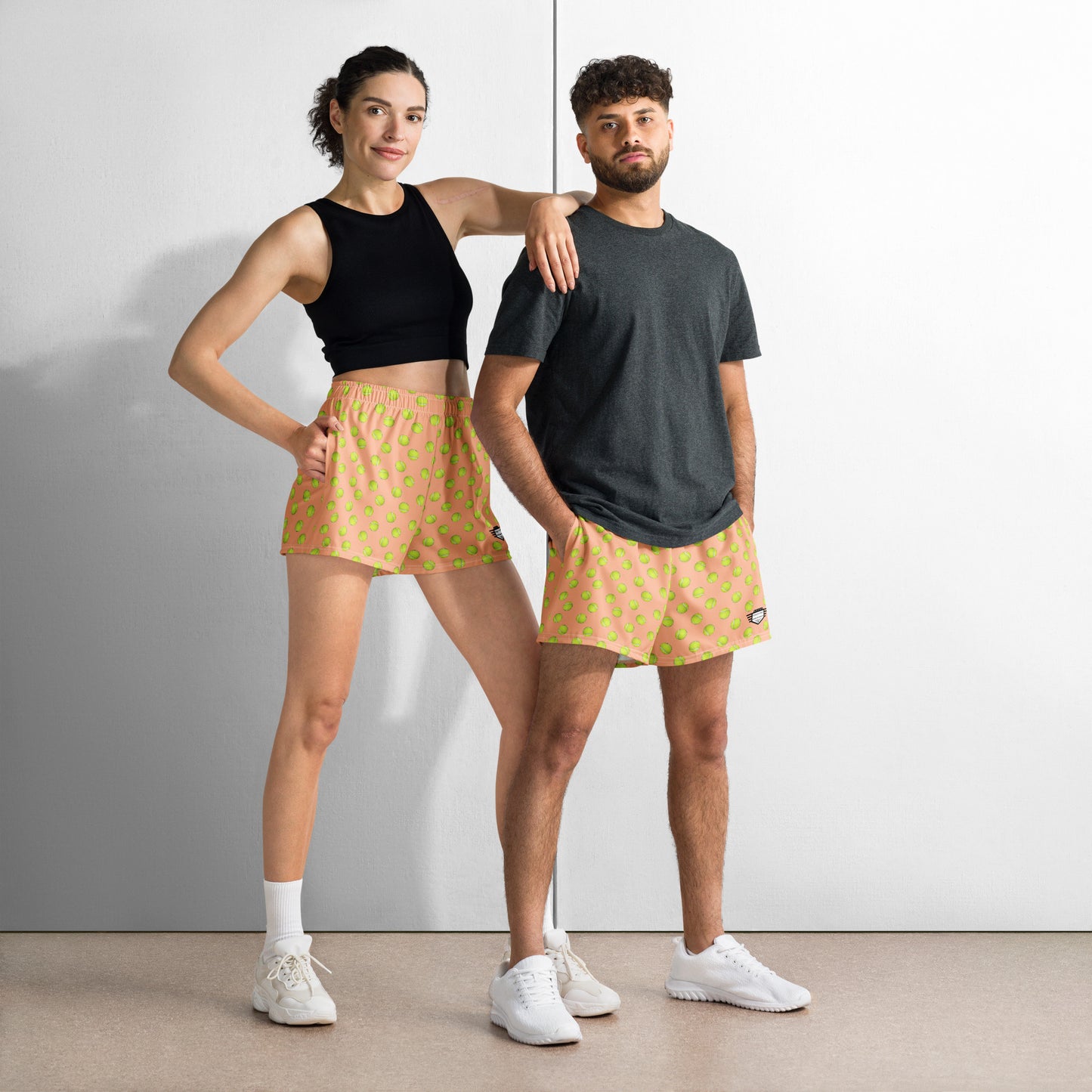 Male and female models posing side-by-side in matching peach tennis ball print athletic shorts, casual style