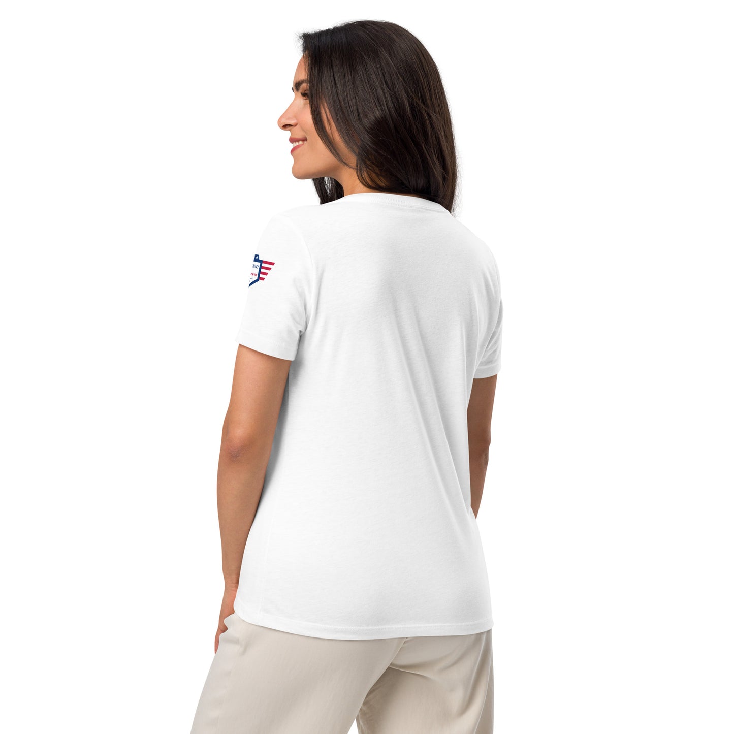 Three-quarter back view of model in plain white V-neck tee showing red-white-blue shoulder patch, relaxed fit with beige pants