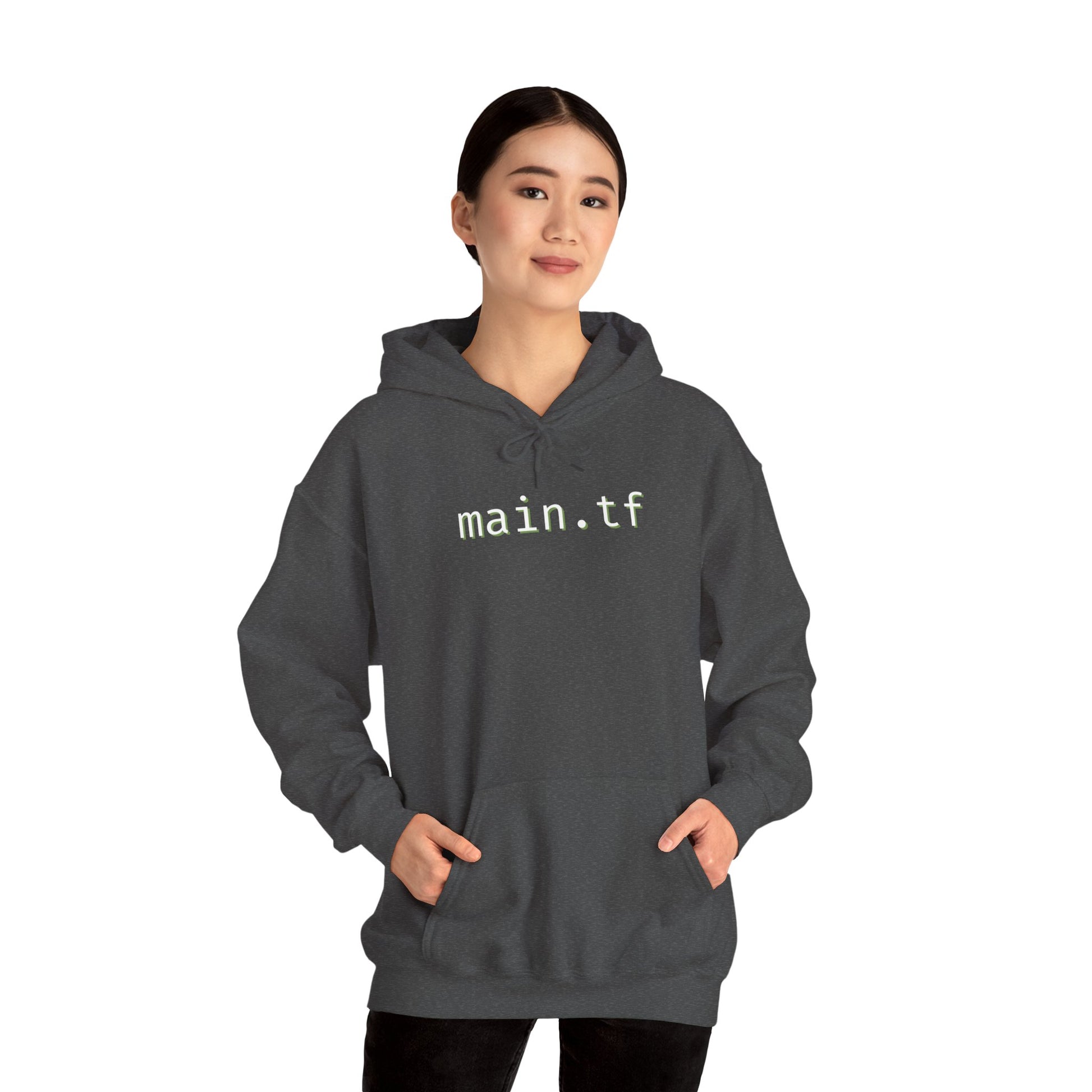 Woman in front of dark heather gray "main.tf" hoodie, light cyan text, hands in pockets
