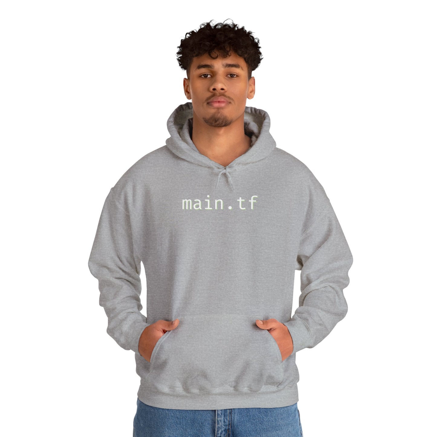 Curly-haired guy in light grey main.tf hoodie, front hands-pocket pose over jeans
