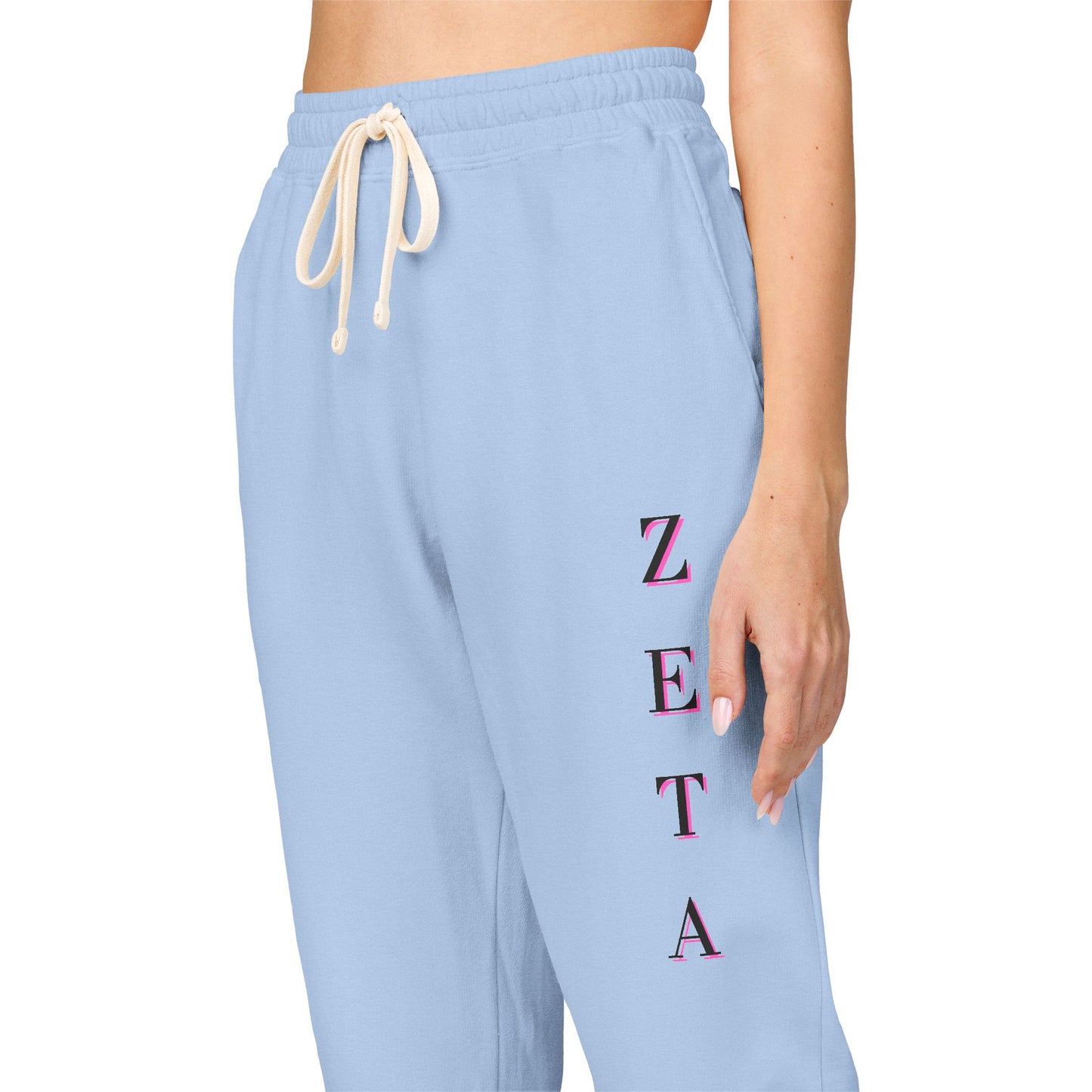 Side close-up of light blue Zeta sweatpants flaunting pink stacked "ZETA" embroidery & drawstrings