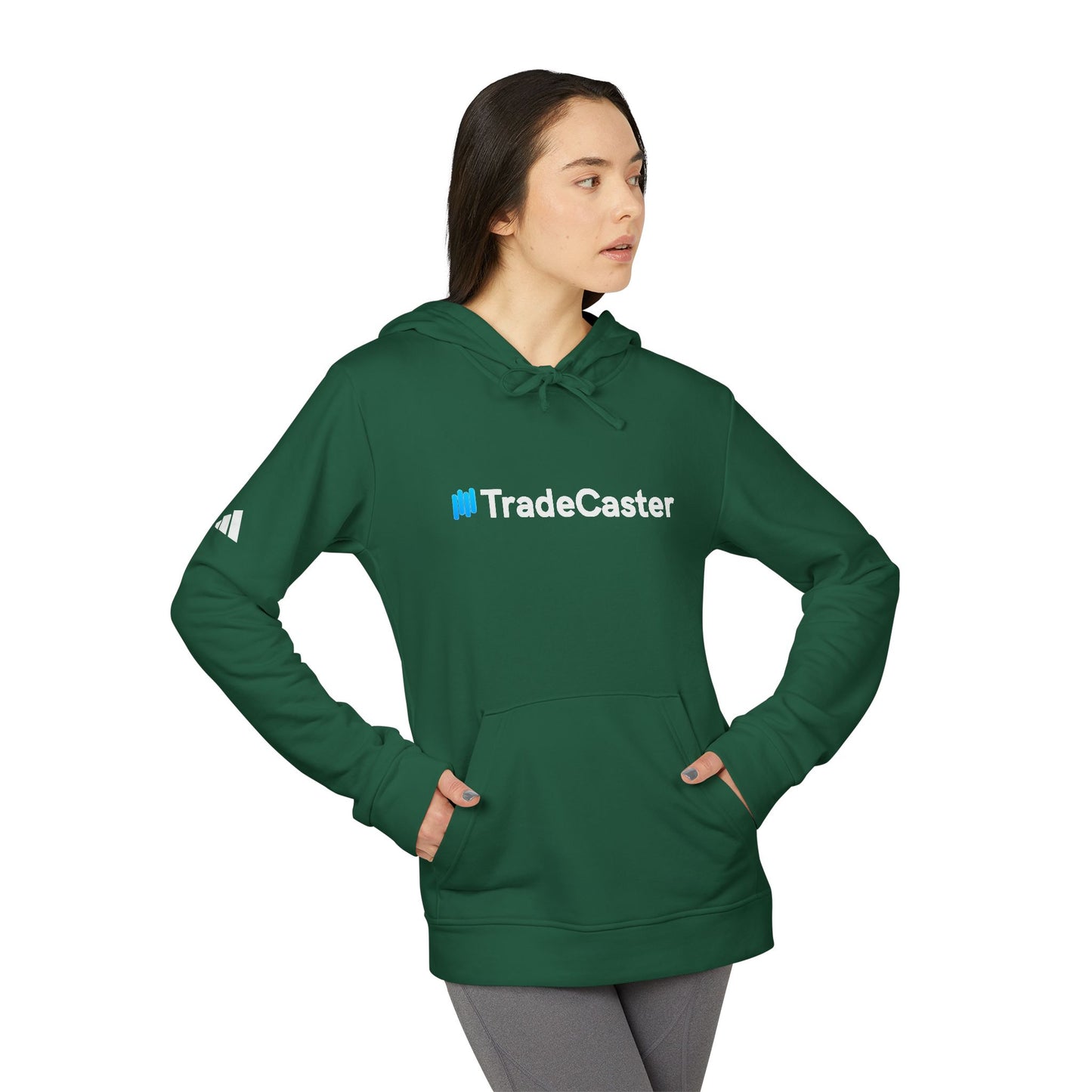 Side angle of woman in green TradeCaster hoodie, Adidas sleeve logo, hands pocketed in grey leggings