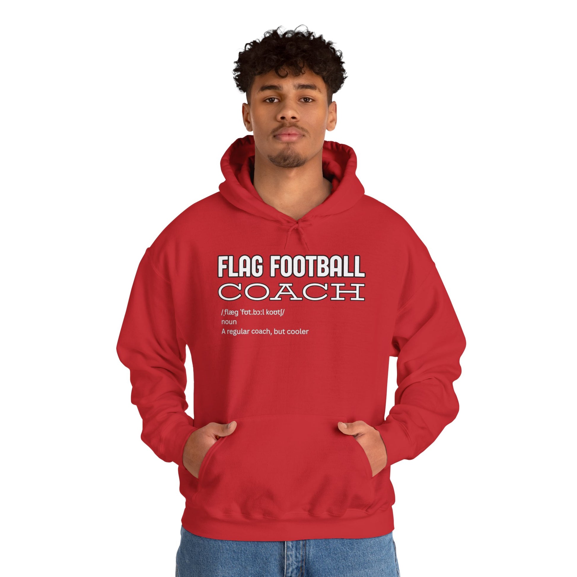 Male model with curly hair wearing red "FLAG FOOTBALL COACH" hoodie, hands in pockets, casual pose