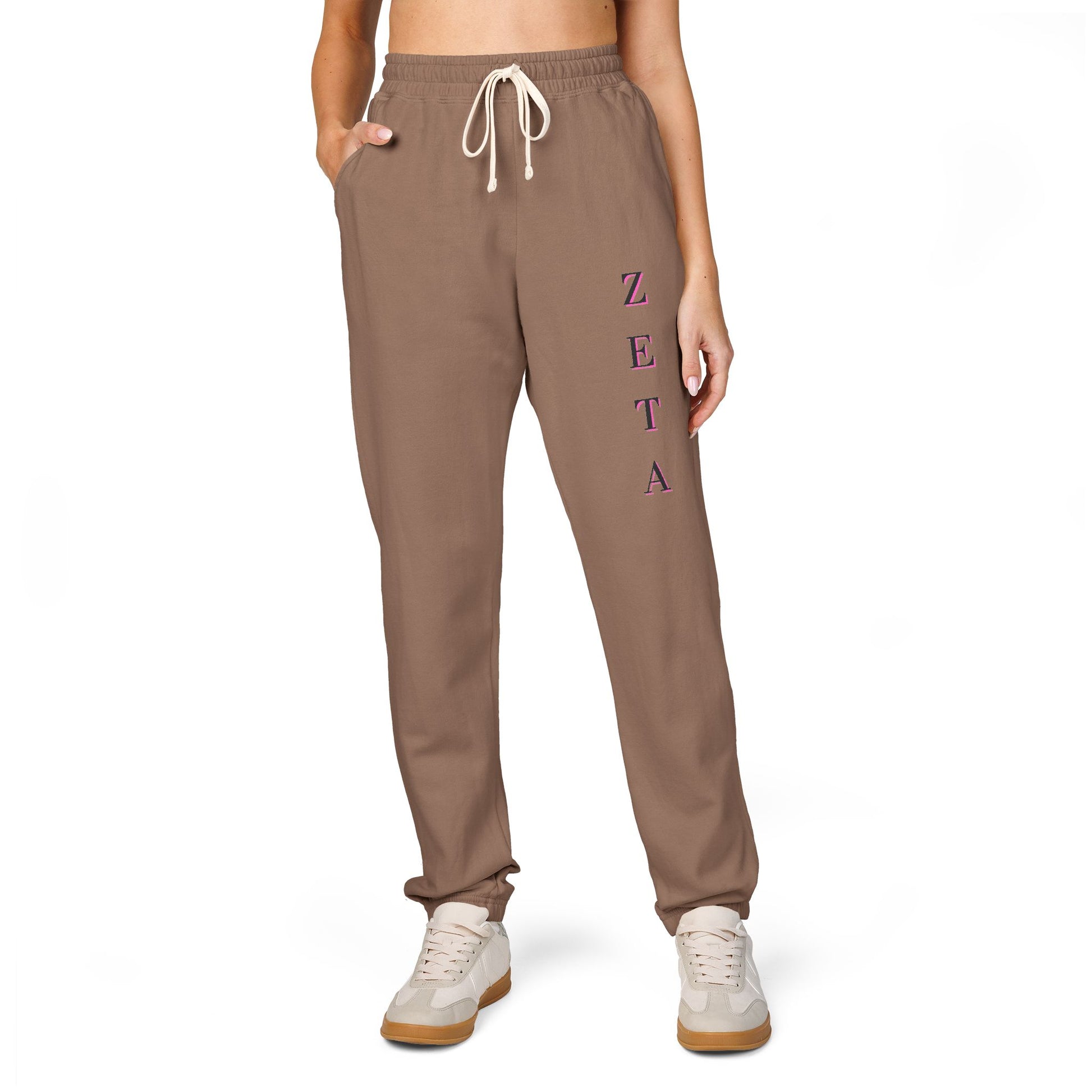 Model front view in espresso Zeta sweatpants, magenta vertical "ZETA" script, crop top, white sneakers