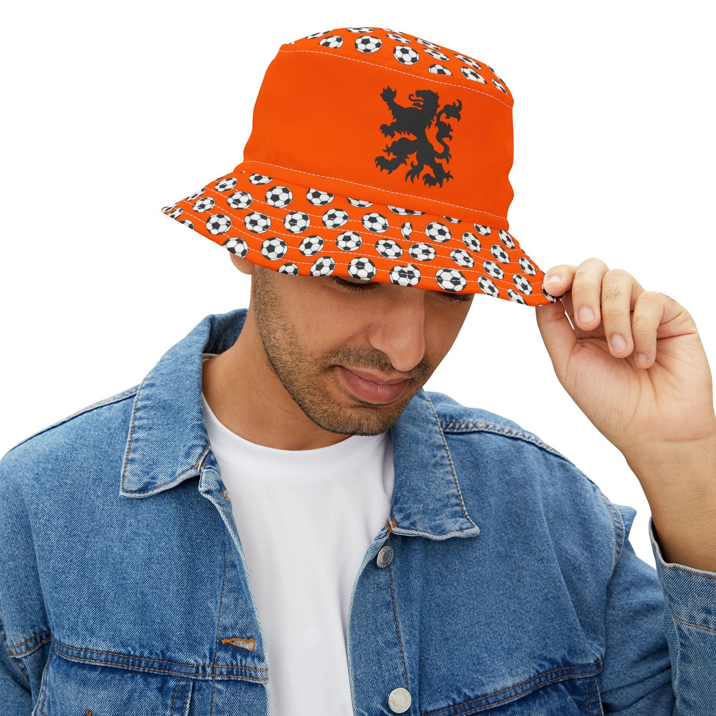 Guy in white tee & denim lifts brim of orange Dutch lion bucket hat, showing black lion & soccer pattern