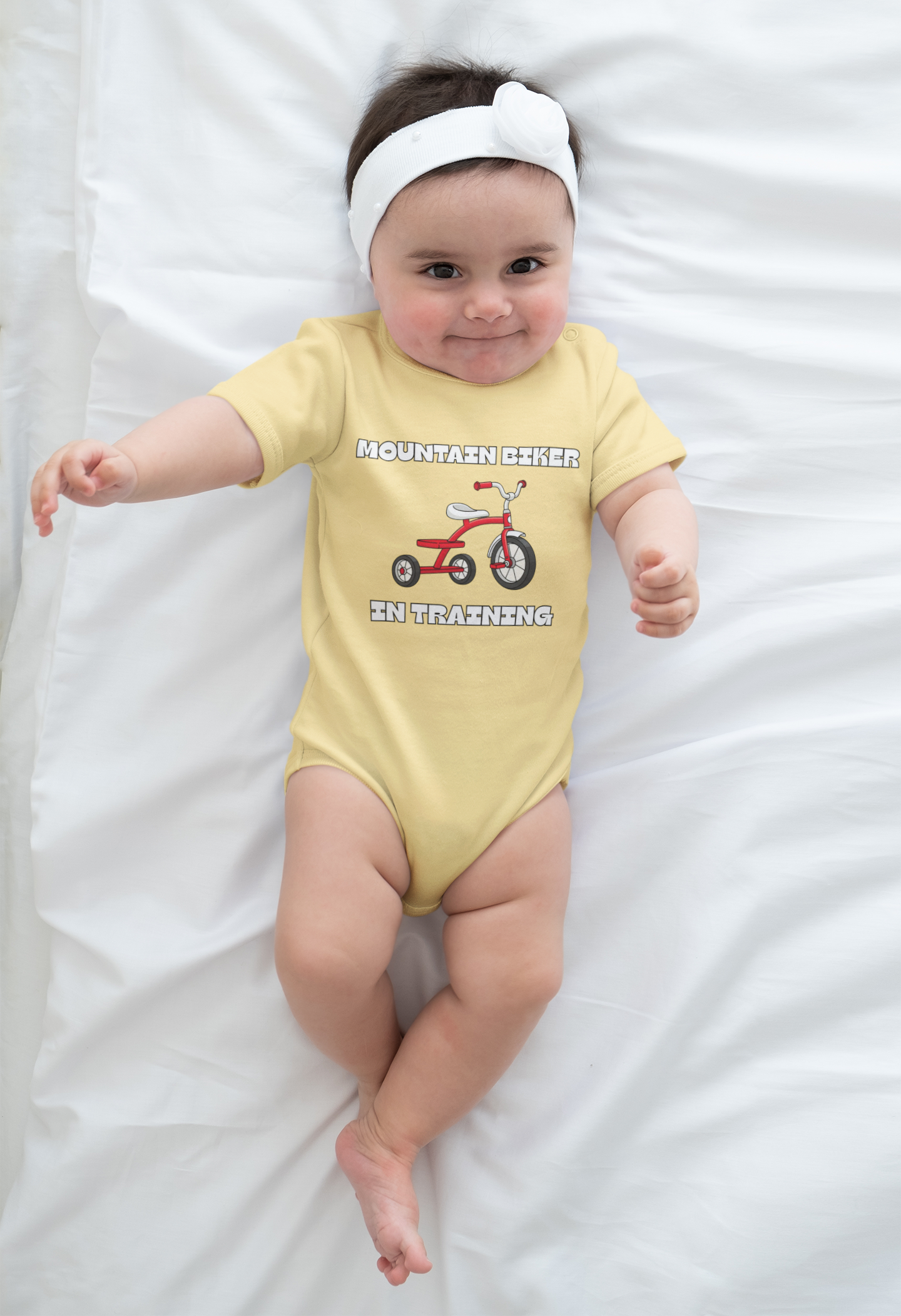 Baby model in green 'Mountain Biker in training' tee with red tricycle - flat lay