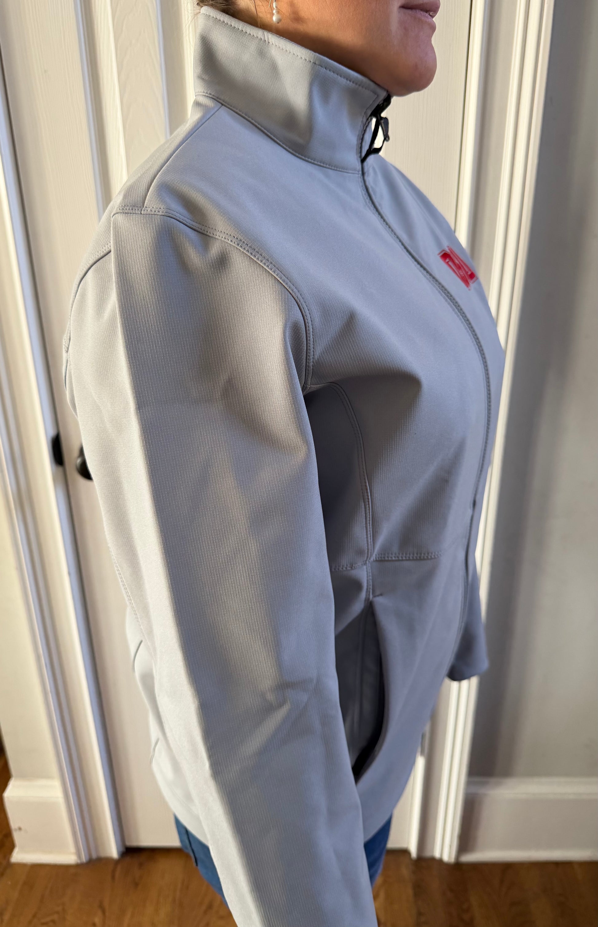 Right side view of light grey OSU softshell on model by door, clean lines no back drama, subtle Buckeye flex