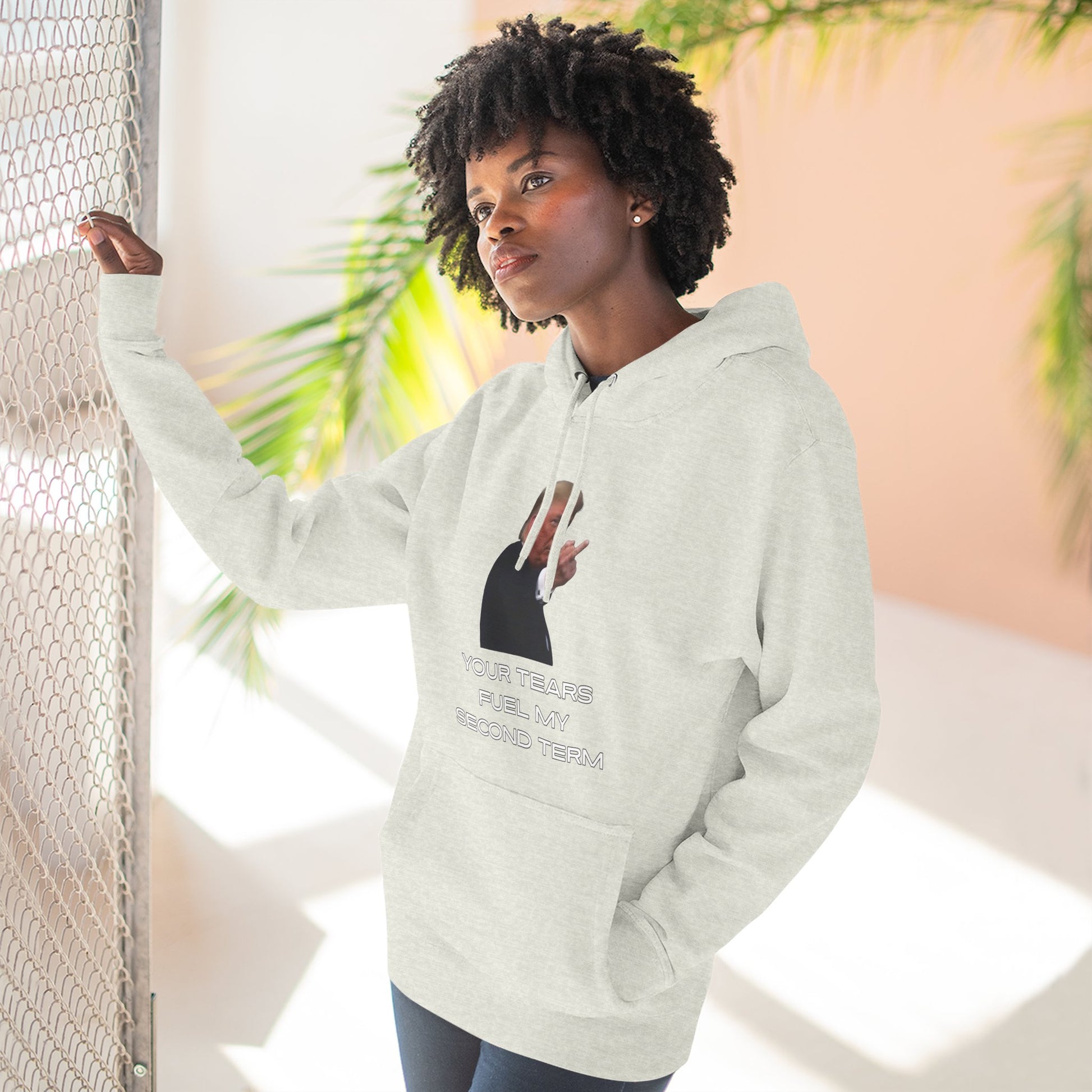 Model leaning against railing in heather gray hoodie, Trump front print with sassy text