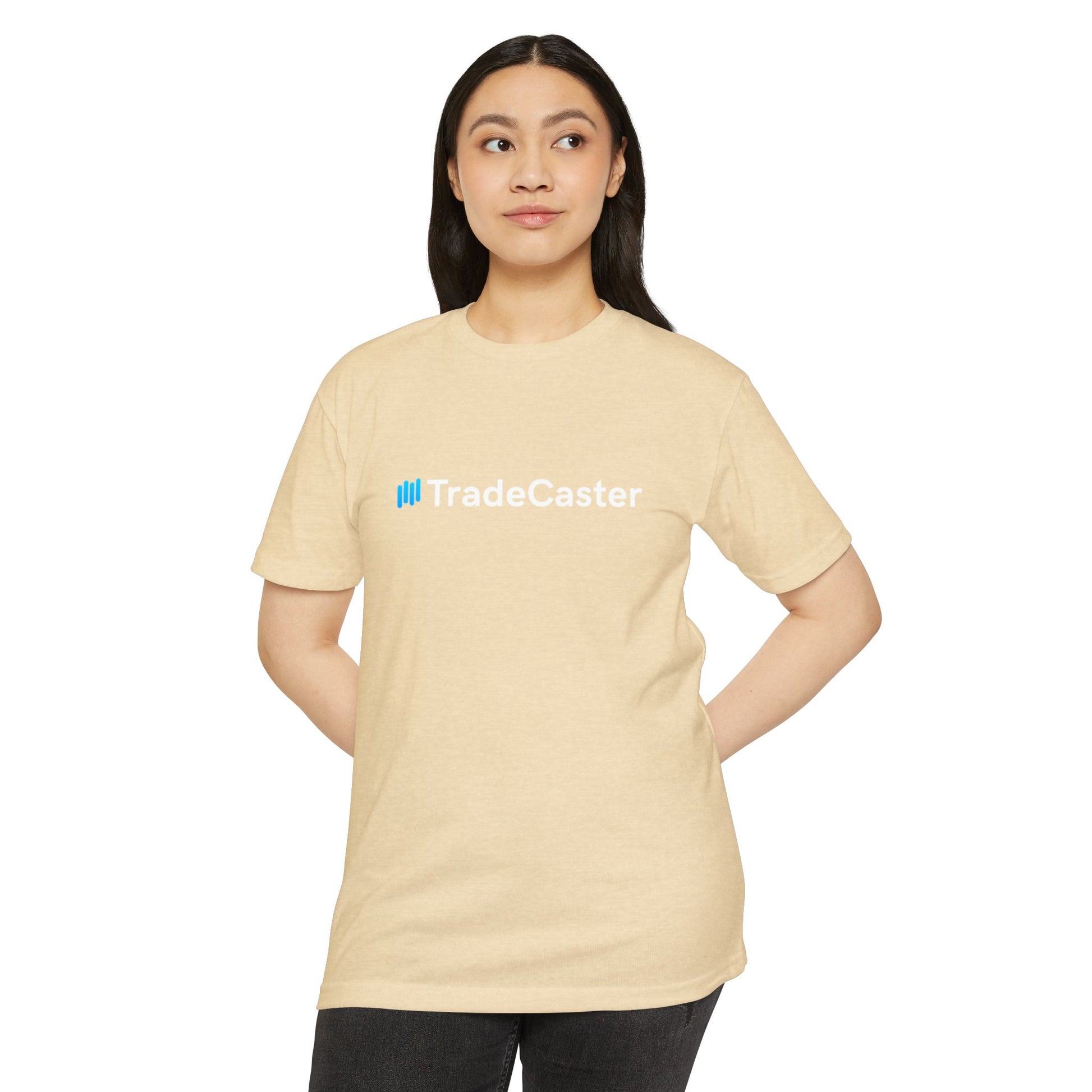 Female model front view rocking beige CVC TradeCaster t-shirt with blue logo, hands on hips in black pants