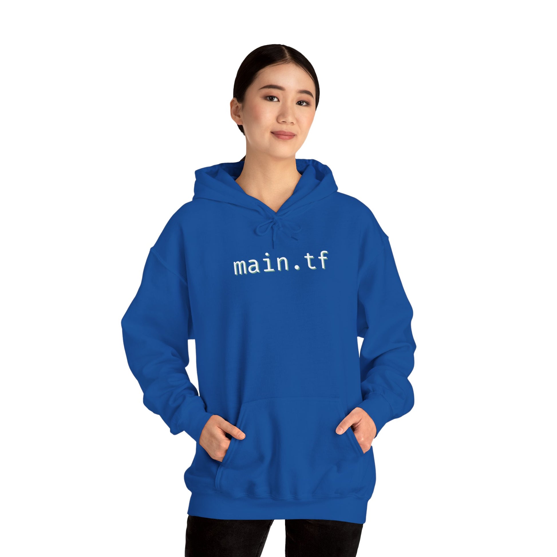 Smiling female model wearing royal blue "main.tf" hoodie, hands in pockets, black pants