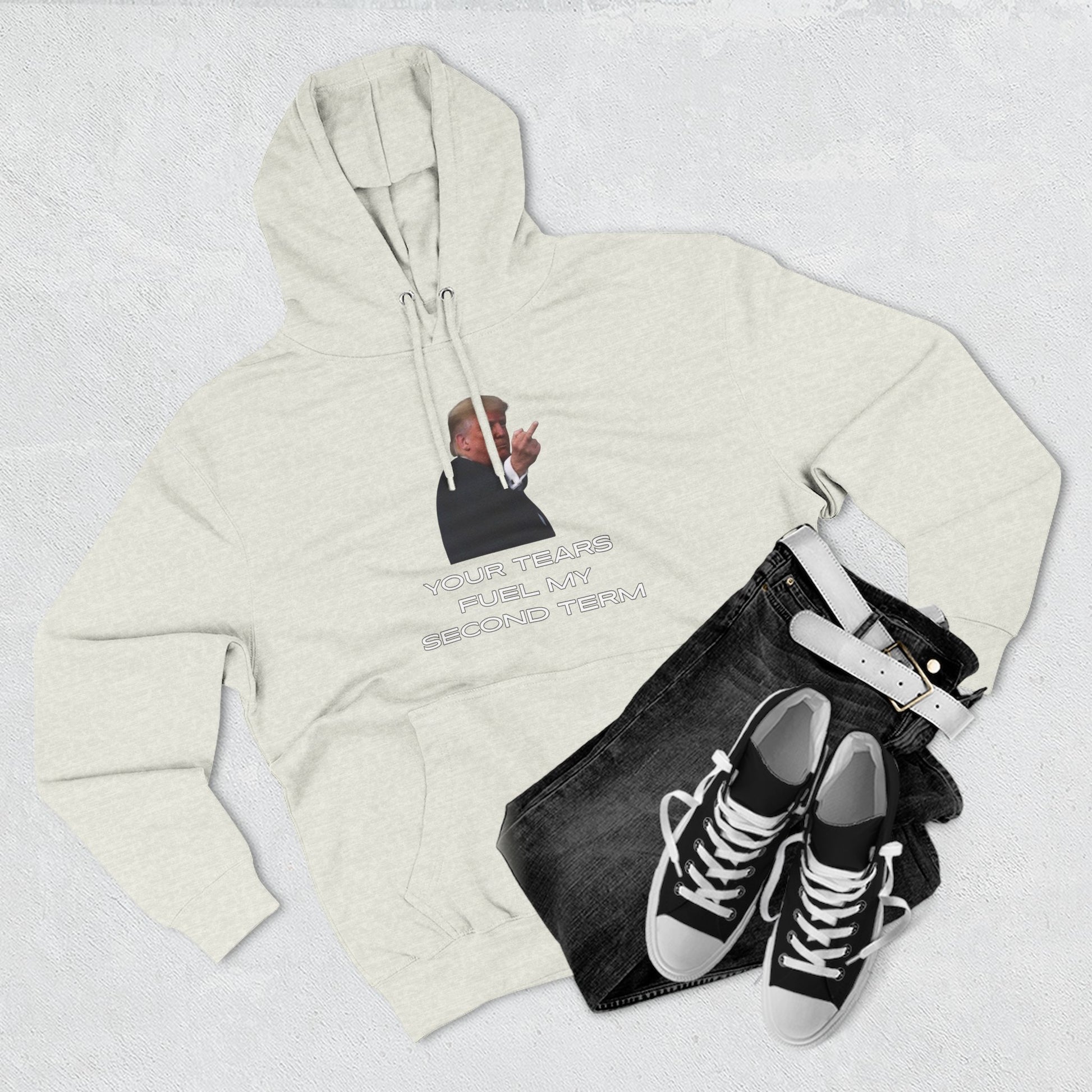 Flat lay heather gray hoodie front with Trump flip-off and "YOUR TEARS FUEL MY SECOND TERM" next to jeans