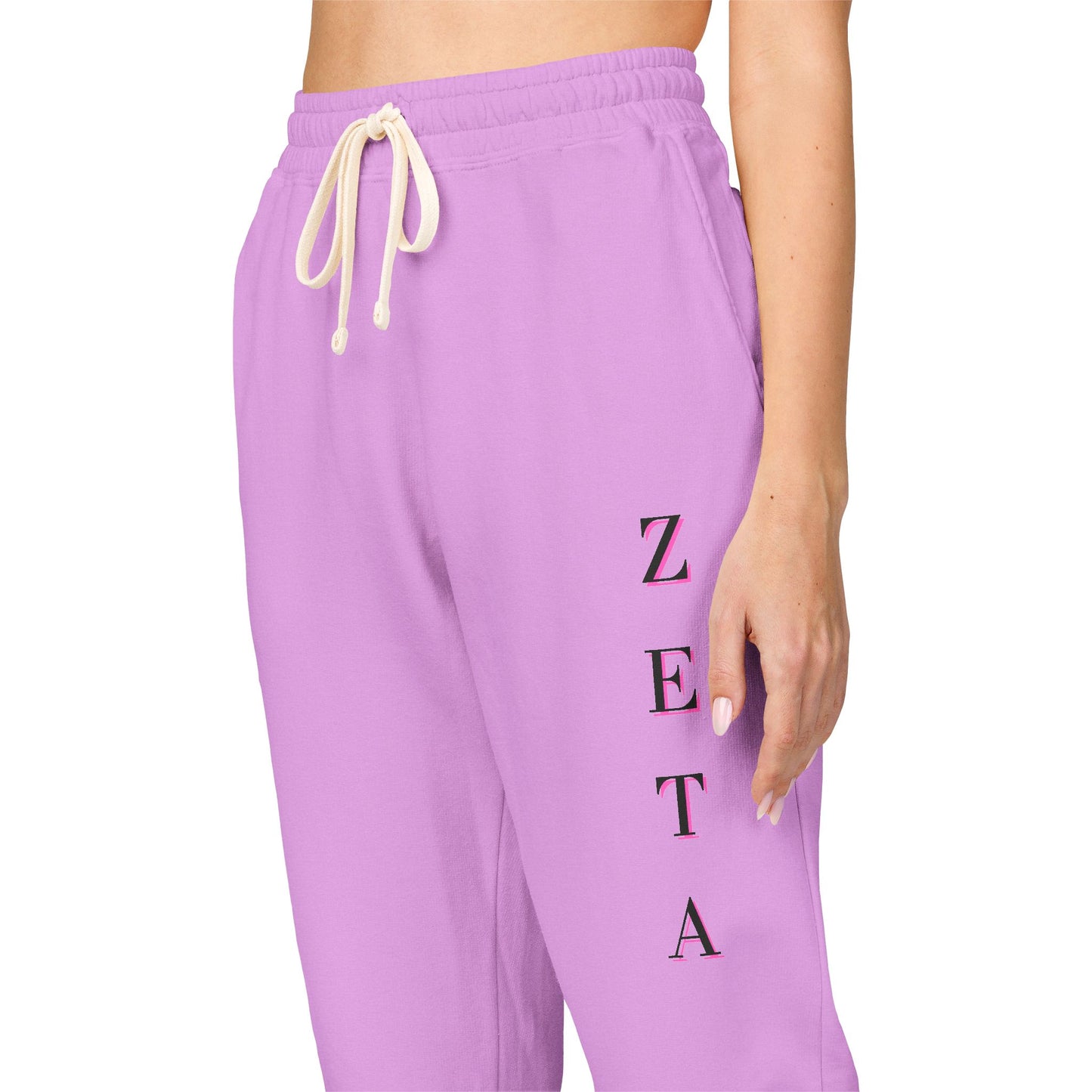 Side view close-up on model leg showing vertical ZETA embroidery on purple sweatpants, drawstring detail