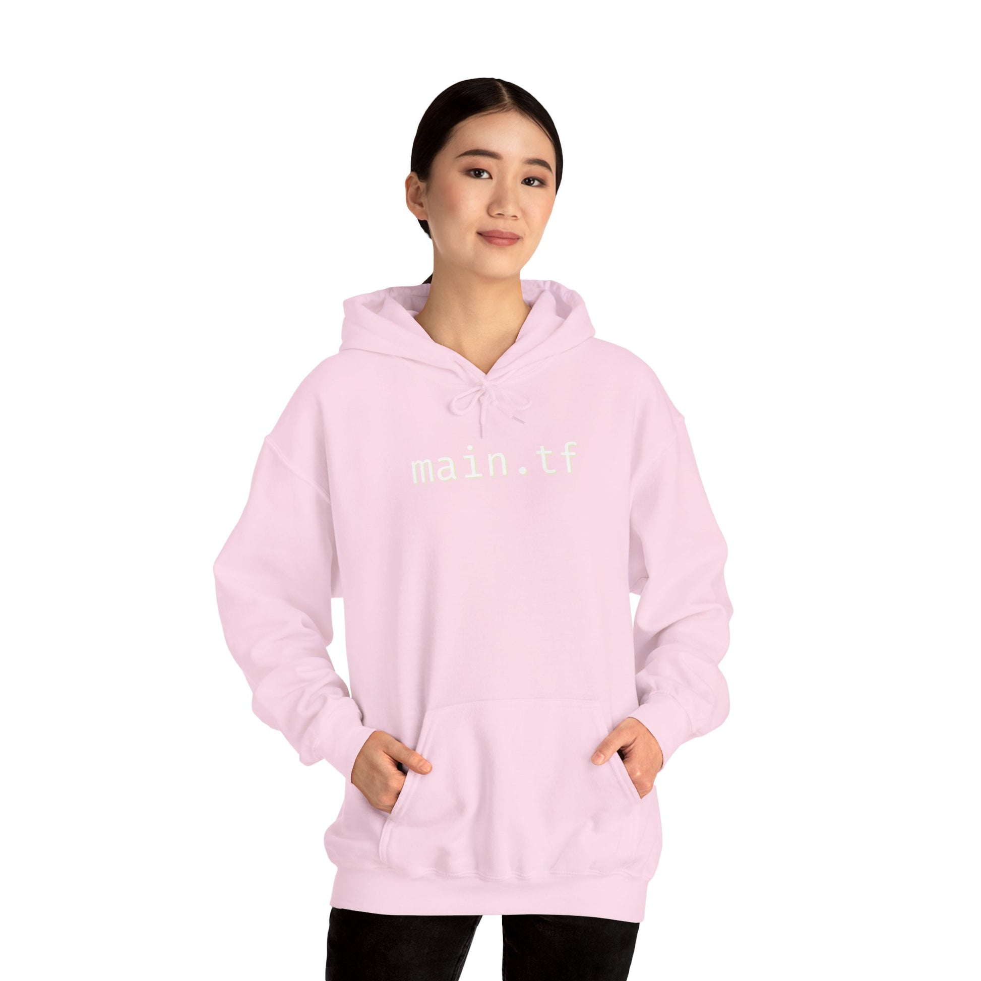 Female model front view in light pink main.tf hoodie, hands in kangaroo pocket