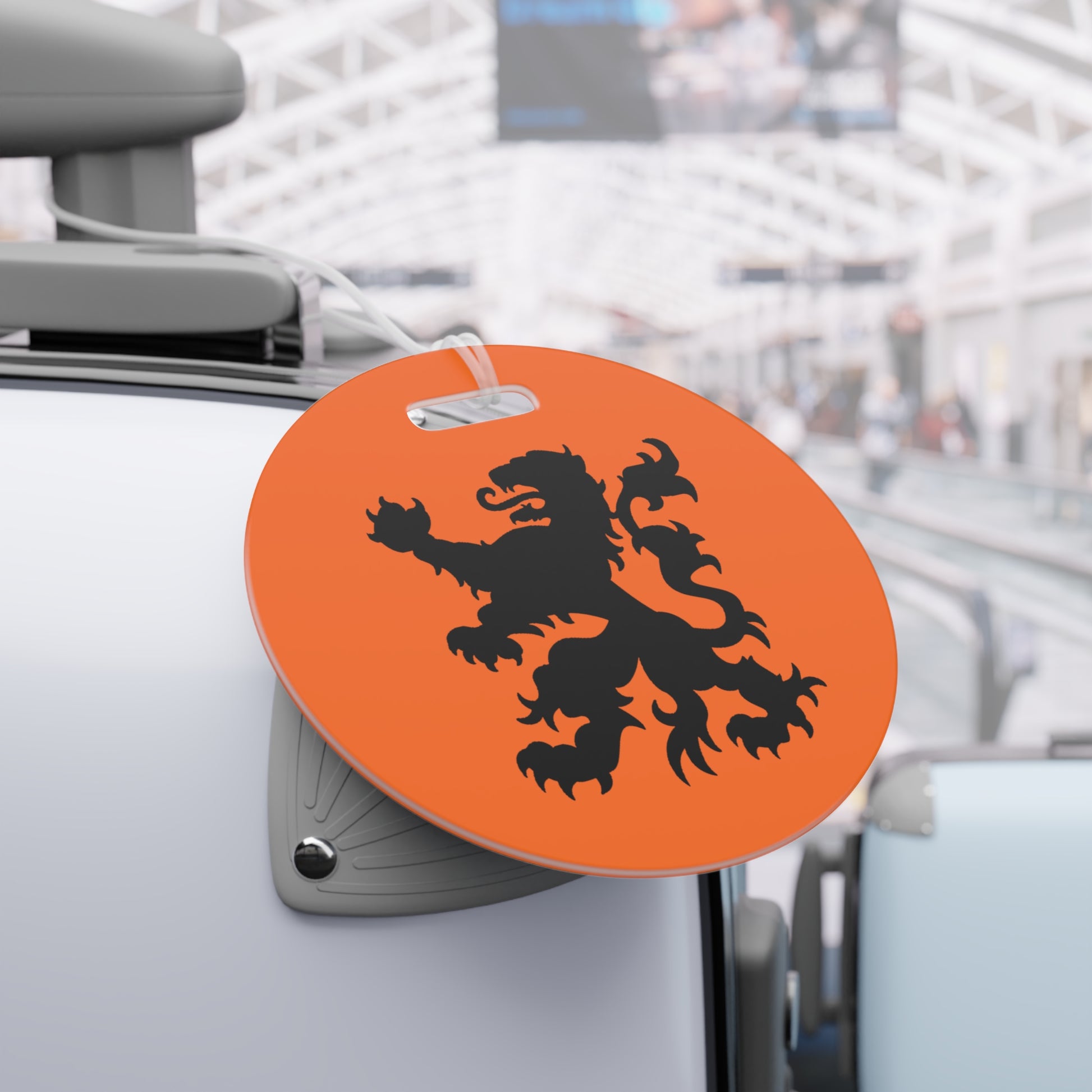 Round orange Dutch Lion tag with black lion on gray suitcase handle amid busy airport baggage claim