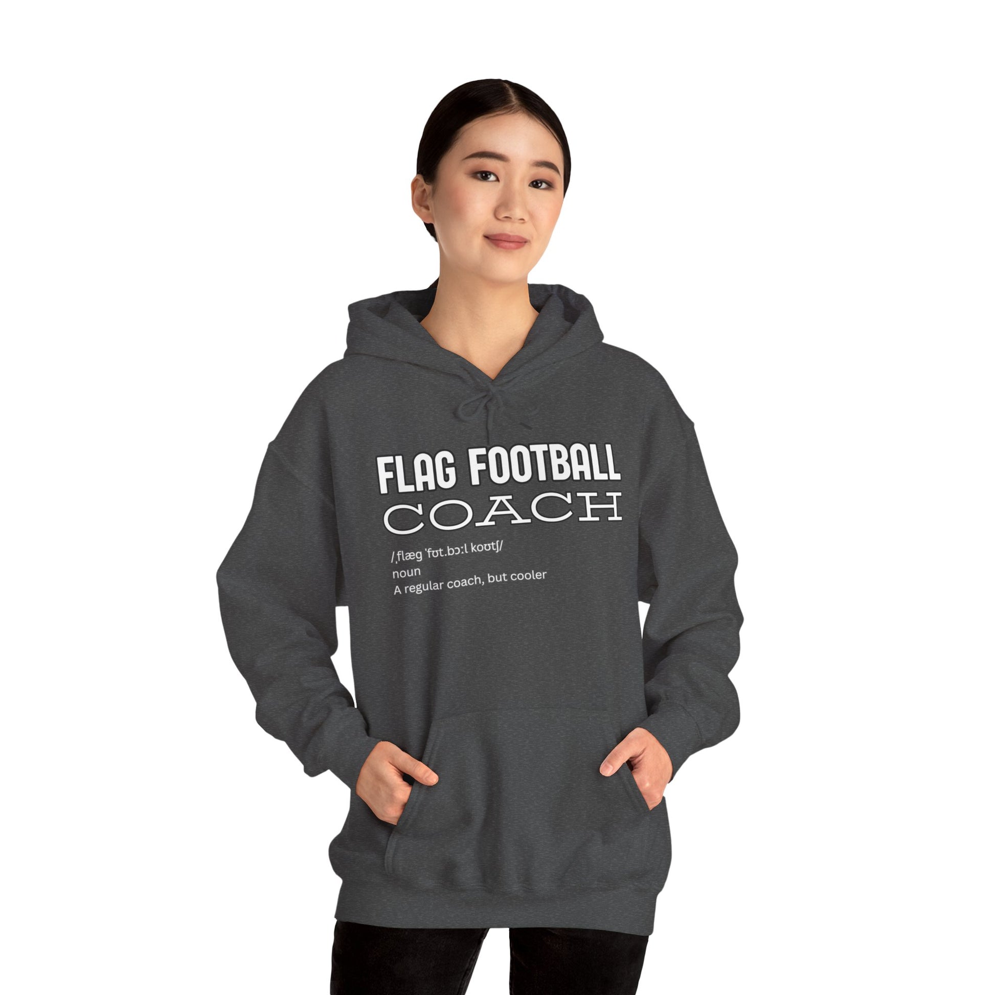 Female model in heather gray Flag Football Coach hoodie, front view with white "Like a regular coach but cooler" print, hands in pockets