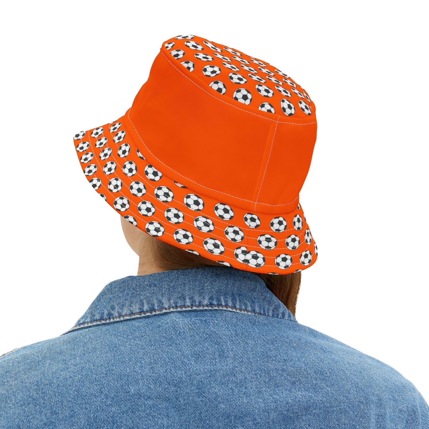 Back view woman in denim & white tee, orange bucket hat brim packed with black & white soccer balls