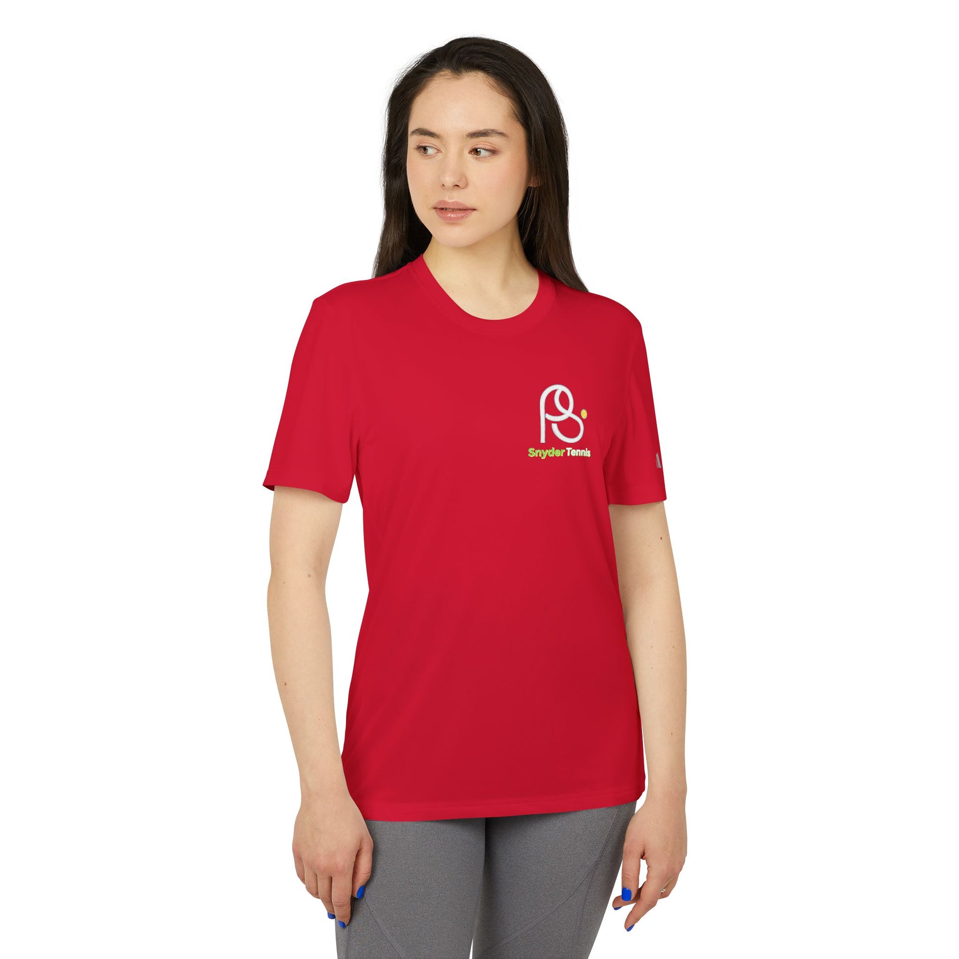 Woman owning Power Red adidas tee, side-front view with PB Tennis logo, sporty gray leggings