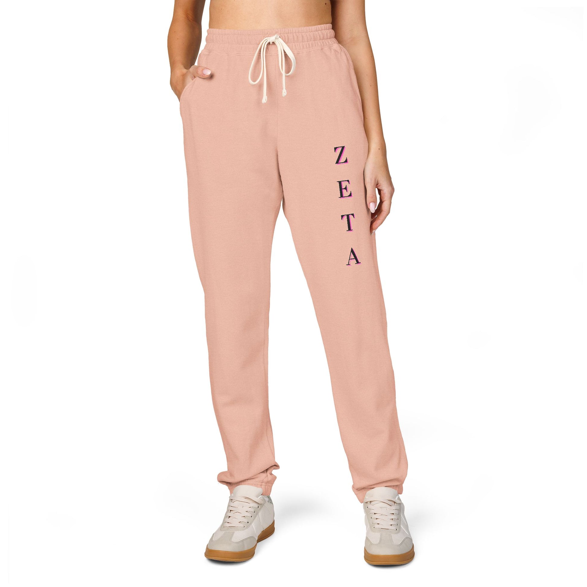 Model fronting peachy Zeta sweatpants, magenta vertical "ZETA" script on leg, crop top, white kicks