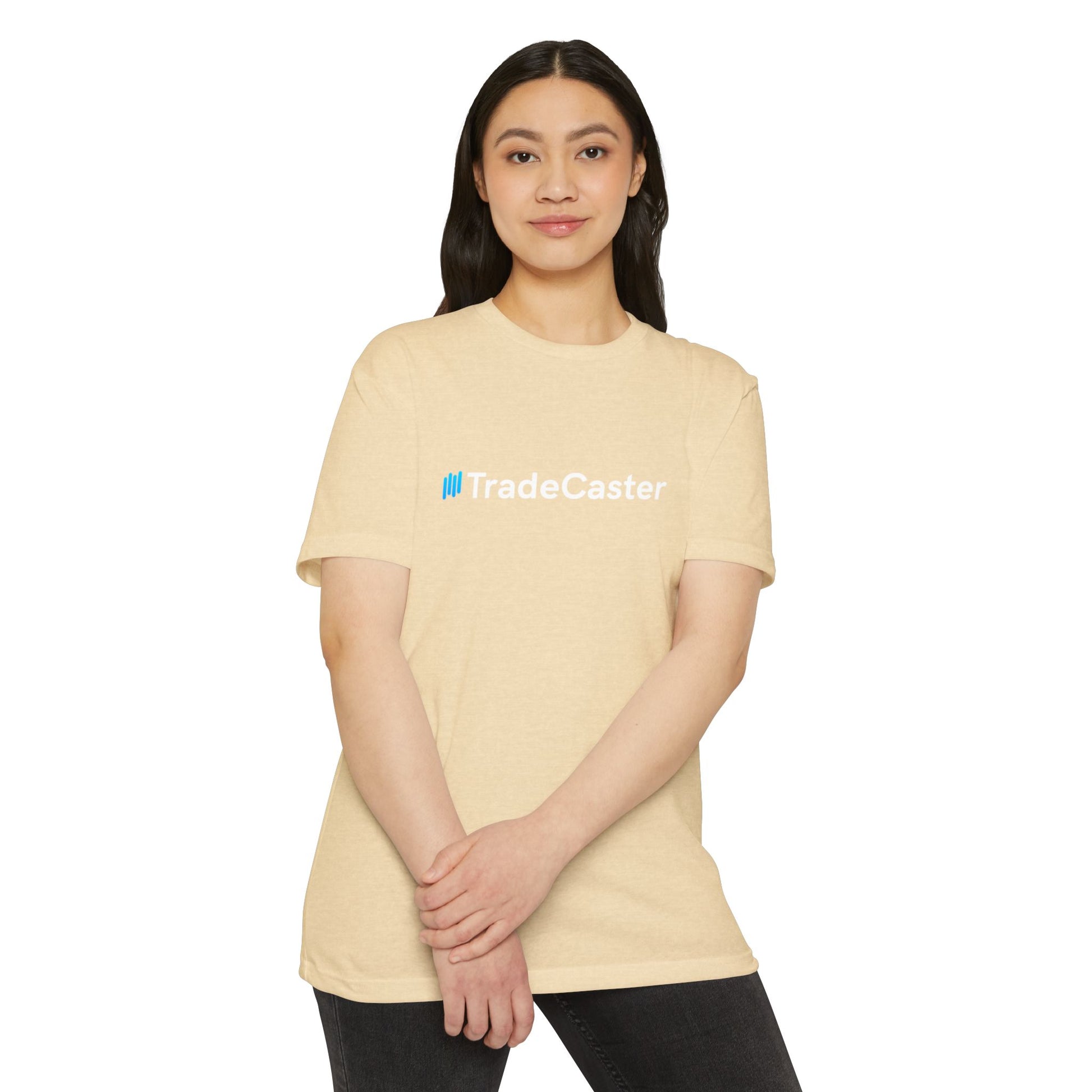 Female model front close-up in beige CVC jersey tee, blue "||TradeCaster" logo, hands crossed