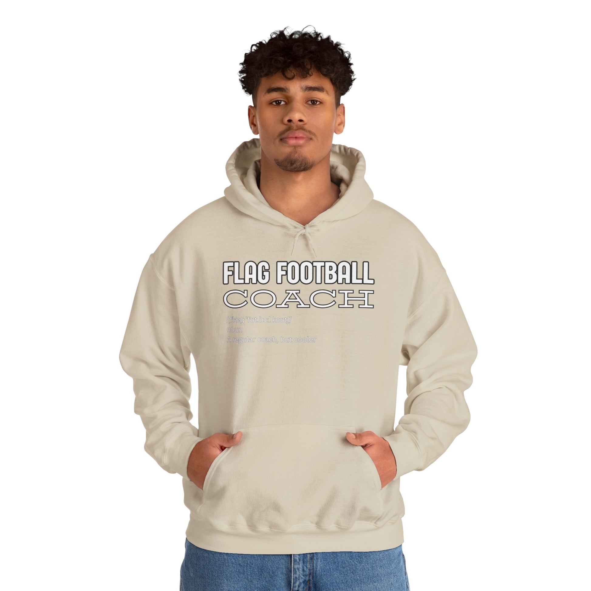 Curly-haired guy owning sand "Flag Football Coach" hoodie front, hands pocketed like a pro