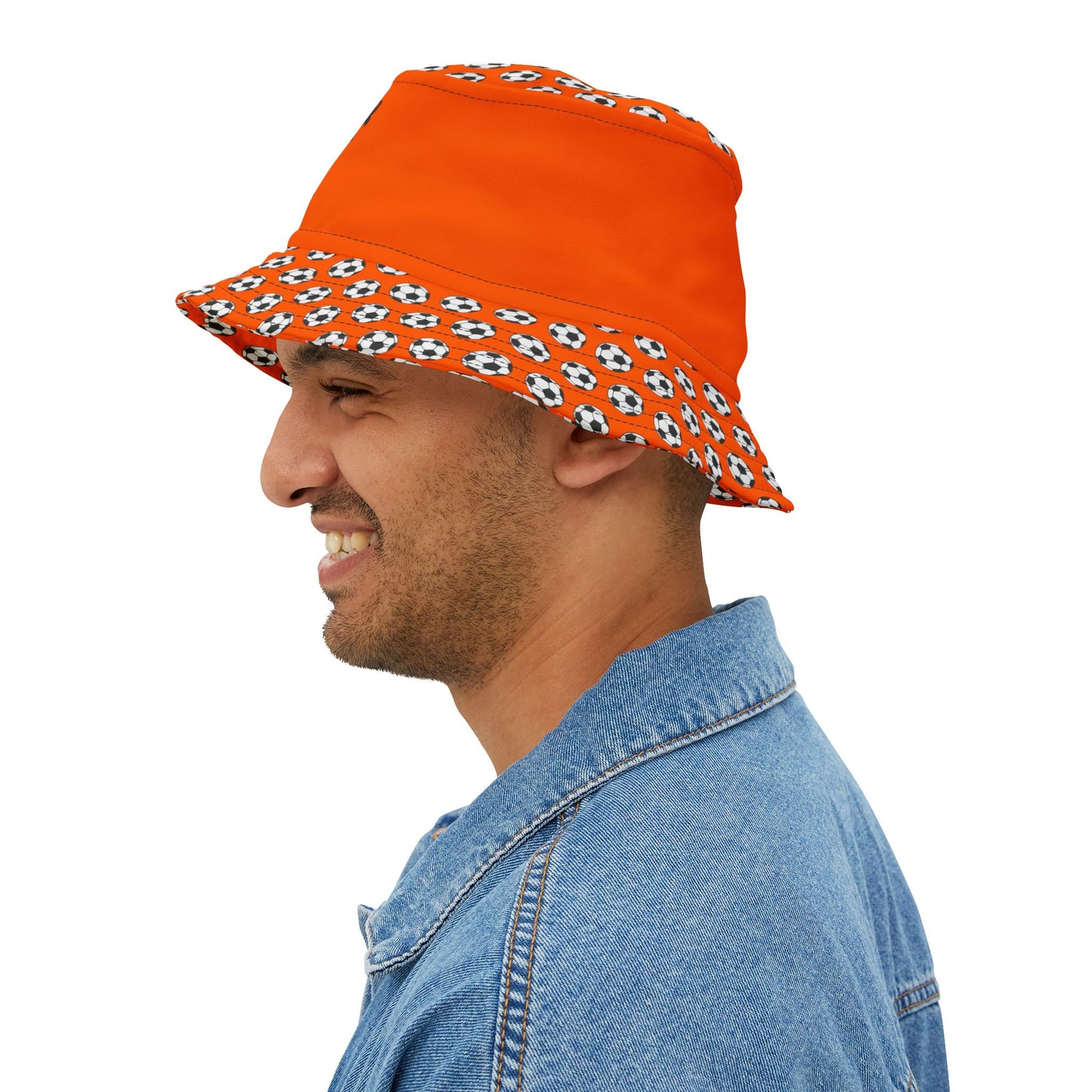 Side profile of smiling guy rocking orange Dutch lion bucket hat with black-and-white soccer ball brim, denim jacket vibes