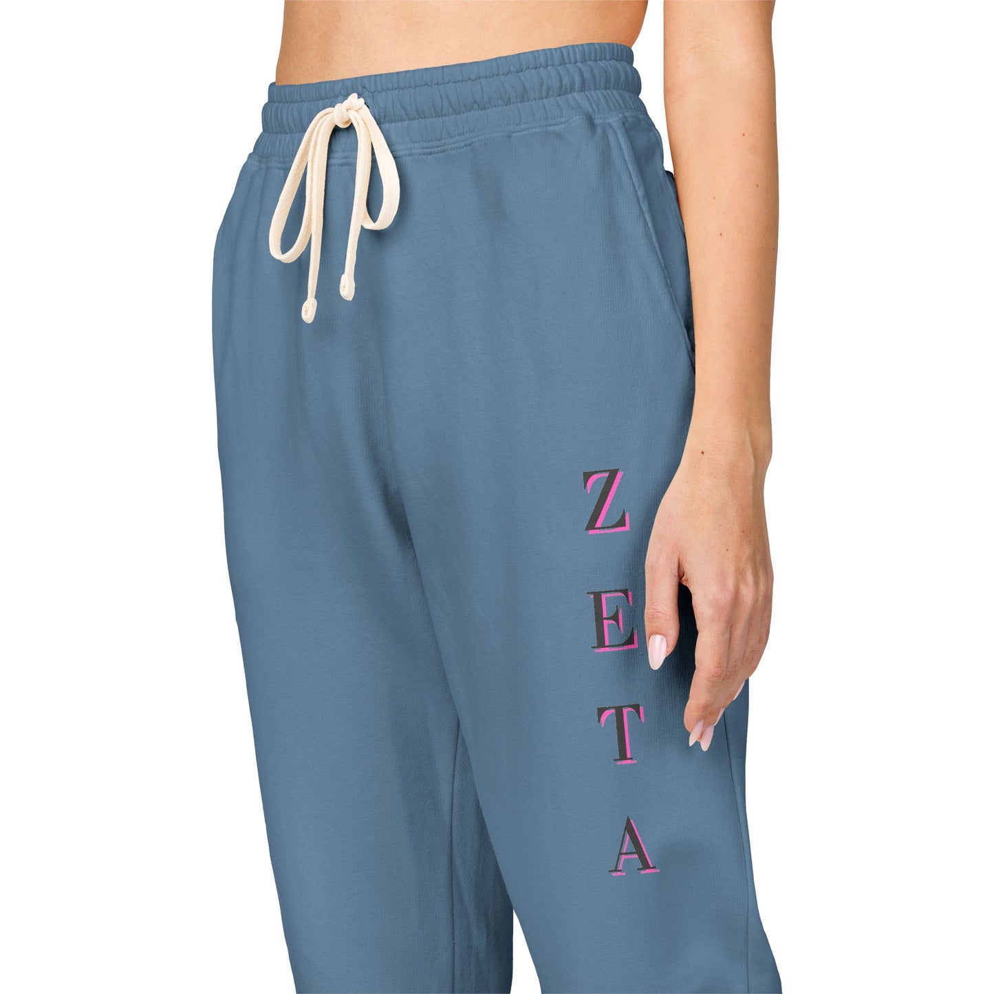 Close-up side of medium blue Zeta sweatpants highlighting bold pink "ZETA" down the leg