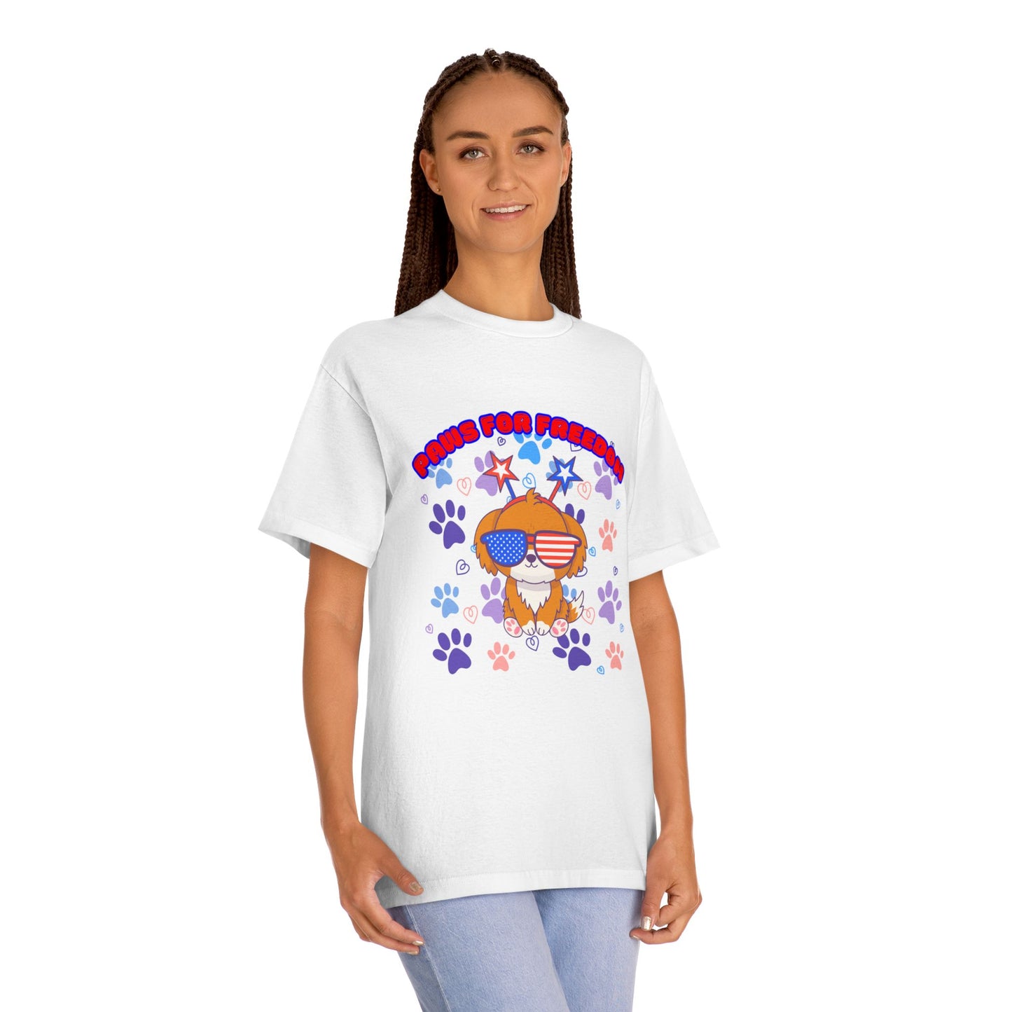 Woman with braids modeling white 'Paws for Freedom' tee front, cartoon dog in flag shades amid paws & stars