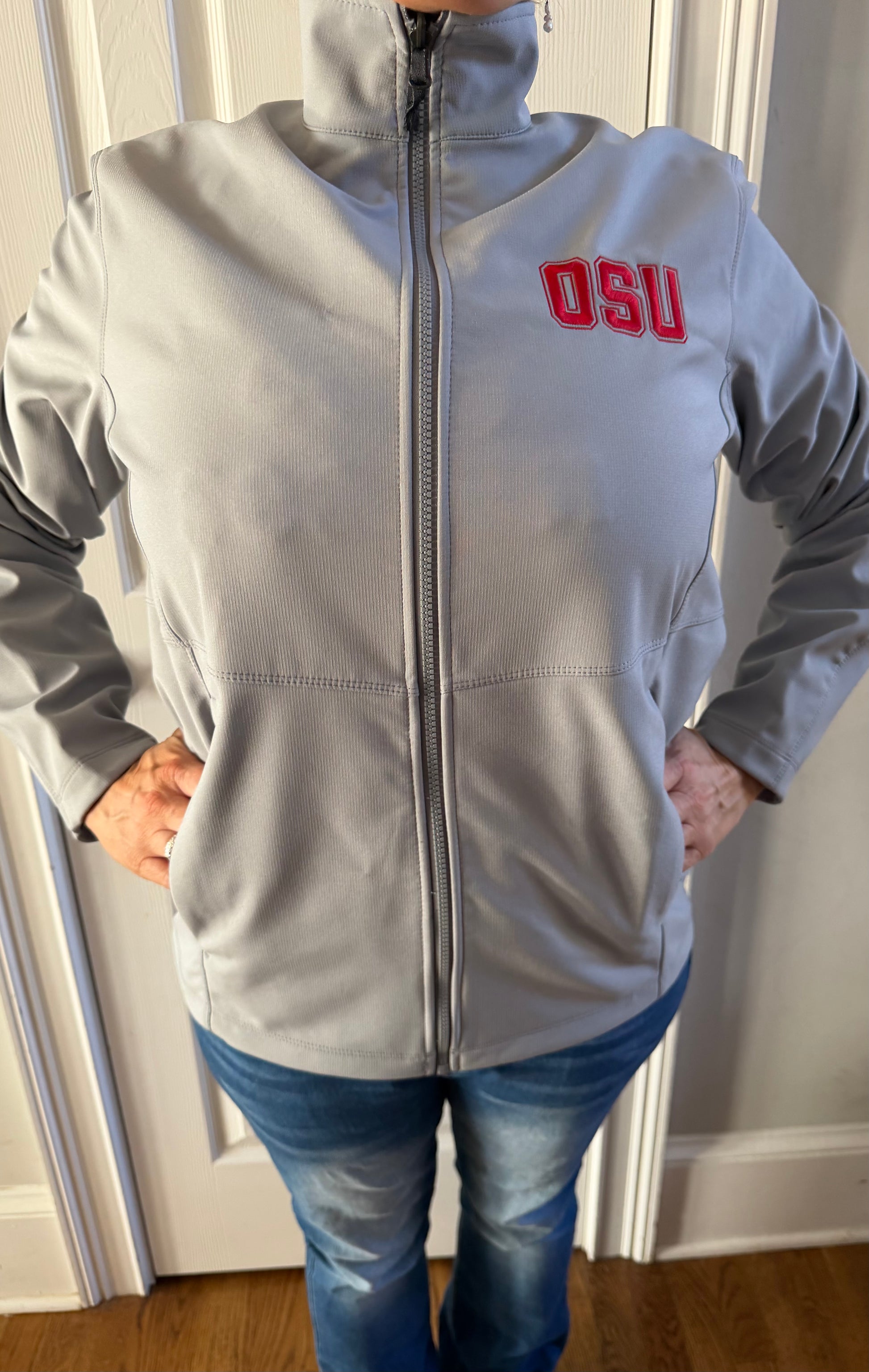 Left side profile of light grey softshell jacket on woman indoors, red OSU embroidery visible, slim fit shine