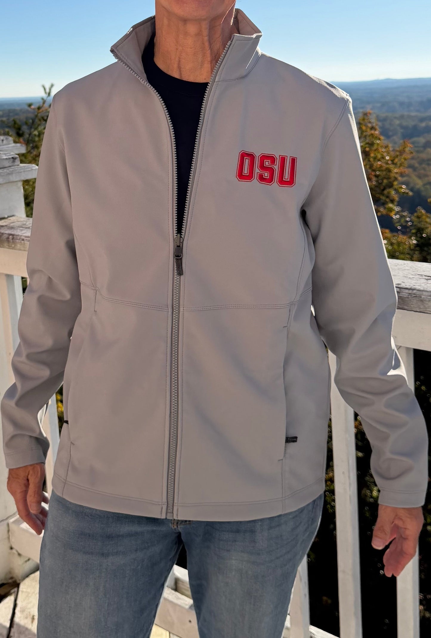 Woman rocks light grey OSU embroidered softshell jacket front view indoors by door, red logo steals the show