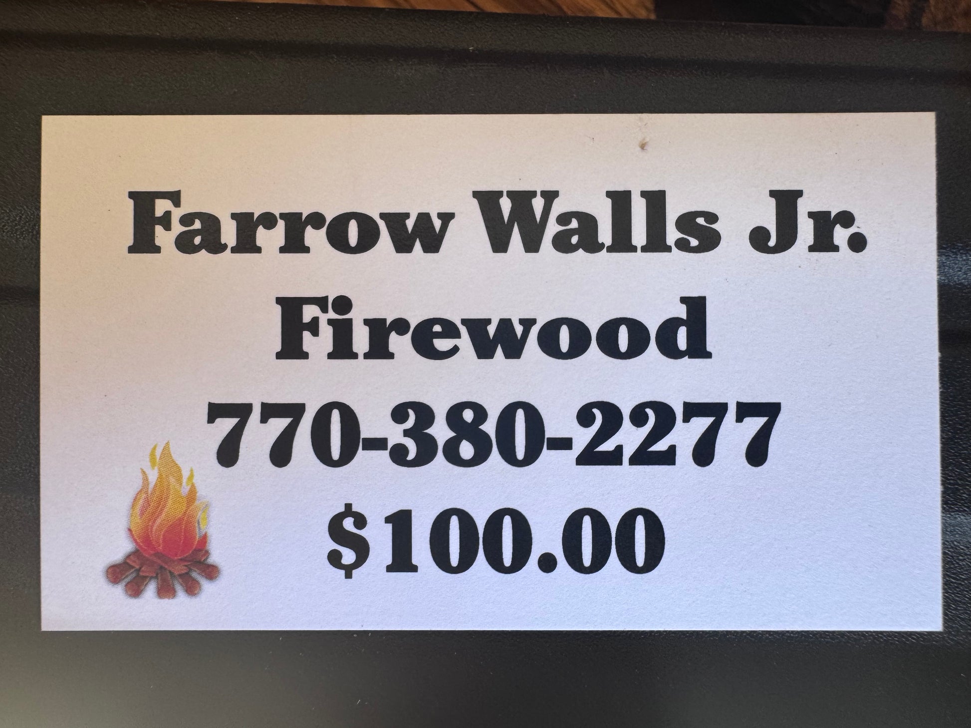Close-up white sign for Farrow Walls Jr. Firewood, 770-380-2277 phone, flame icon, $100.00 price