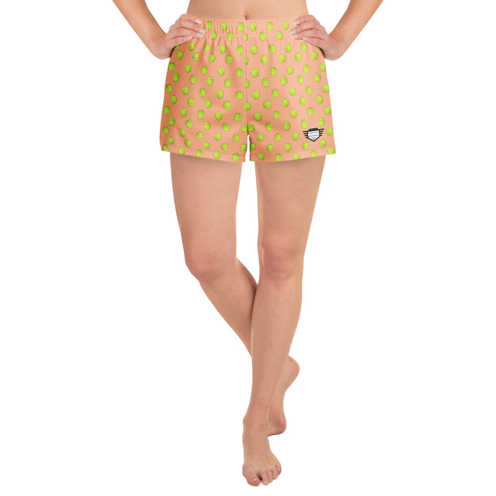 Front view of model in peach athletic shorts with all-over green tennis ball print, hands on hips, cheeky 2.5" inseam