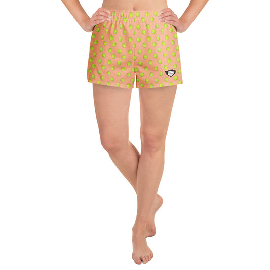 Front view of model in peach athletic shorts with all-over green tennis ball print, hands on hips, cheeky 2.5" inseam