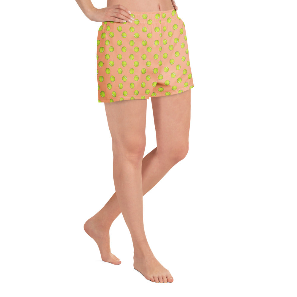 Three-quarter front view of model strutting in peach tennis ball print shorts, left leg forward, playful vibe