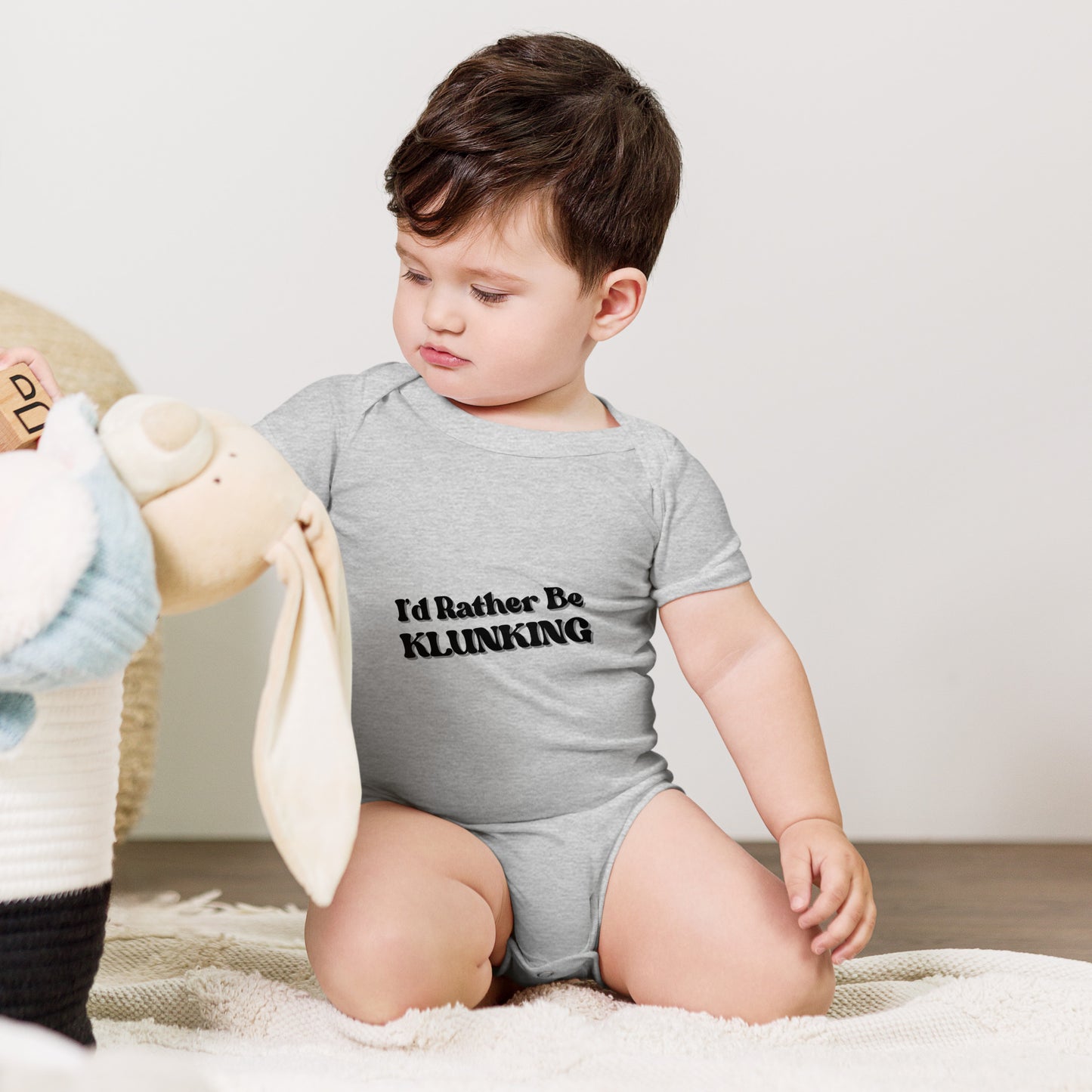 Baby hugging teddy in heather gray "I’d Rather Be Klunking" short sleeve onesie, chill vibes