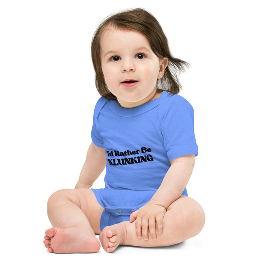 Grinning baby sitting in light blue "I’d Rather Be Klunking" onesie, short sleeves and snaps visible