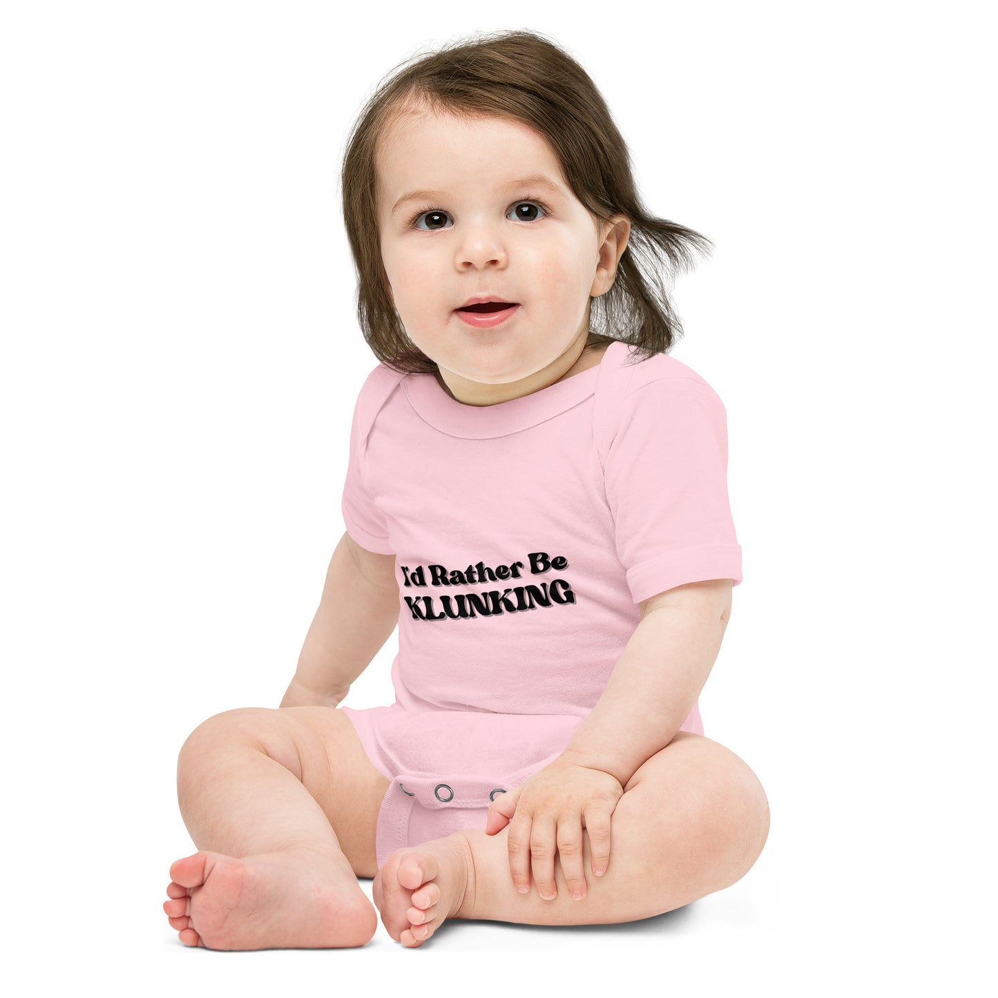 Baby model sitting in light pink "I’d Rather Be Klunking" short sleeve onesie, front view with black text