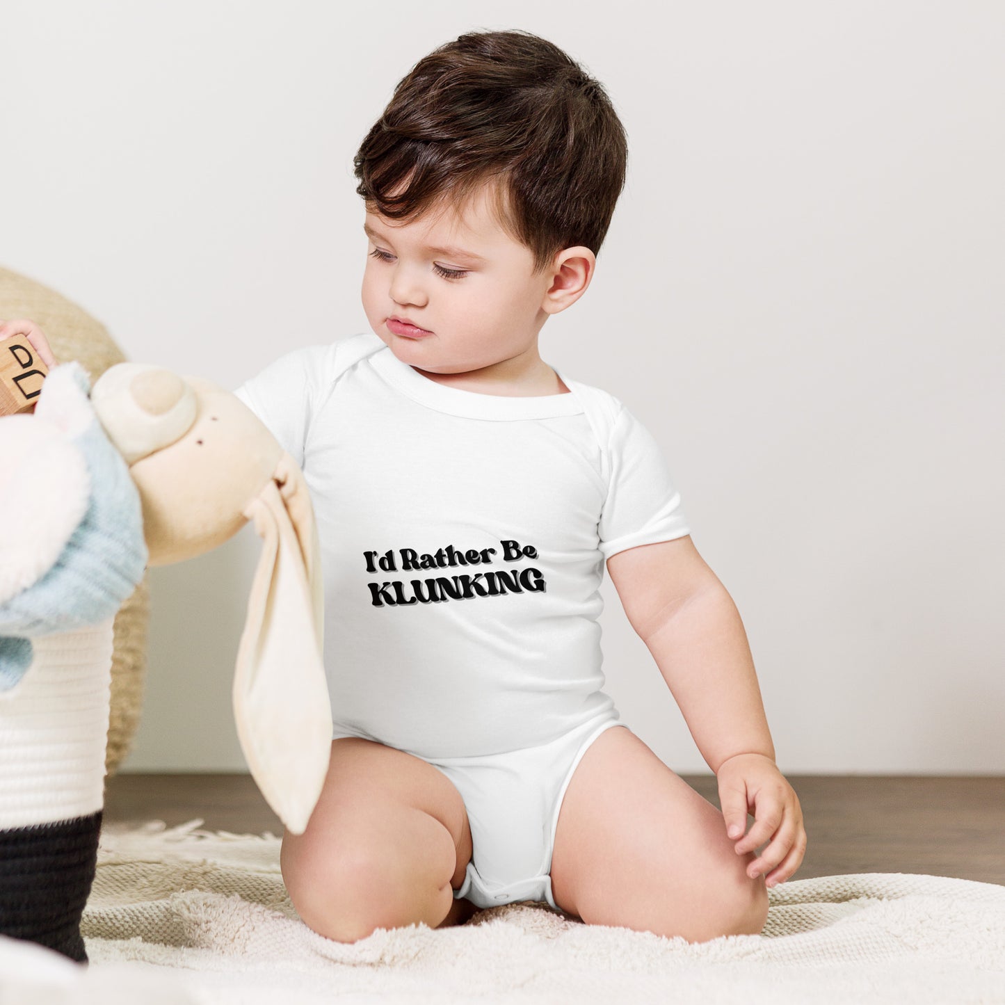 Baby with teddy bear in white "I’d Rather Be Klunking" onesie, tiny explorer look