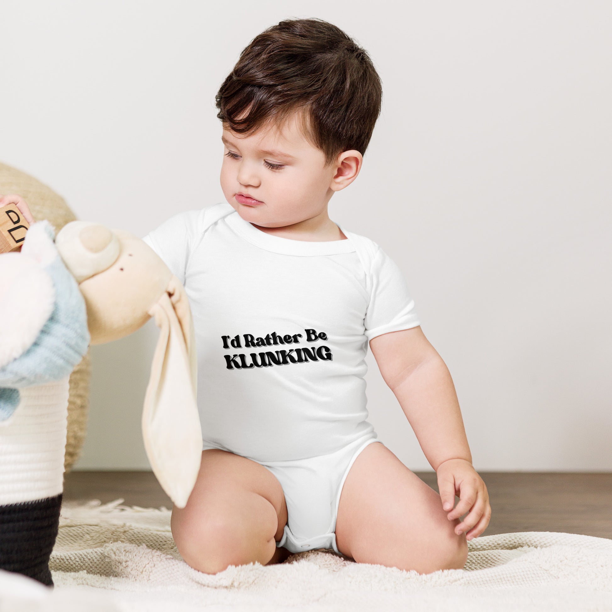 Baby with teddy bear in white "I’d Rather Be Klunking" onesie, tiny explorer look