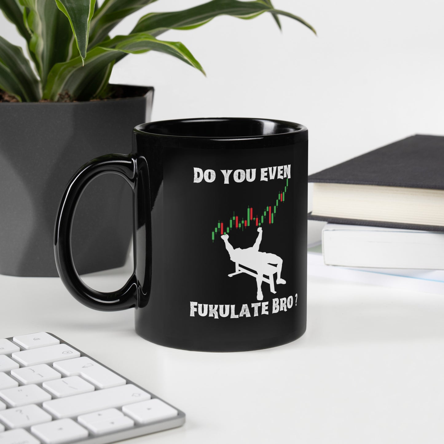 Desk vibe with glossy black "Do You Even FUKULATE" mug, green plant left, books and keyboard right