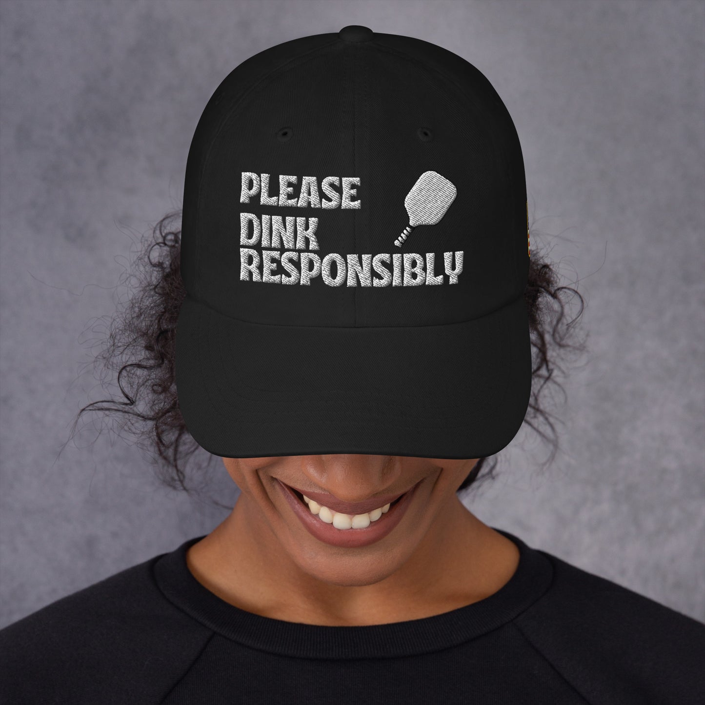 Front view of black dad hat on smiling model, white "PLEASE DINK RESPONSIBLY" embroidery with pickleball paddle icon