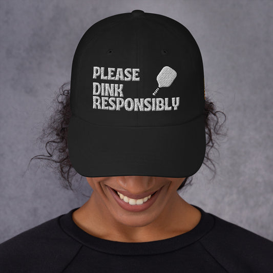 Front view of black dad hat on smiling model, white "PLEASE DINK RESPONSIBLY" embroidery with pickleball paddle icon