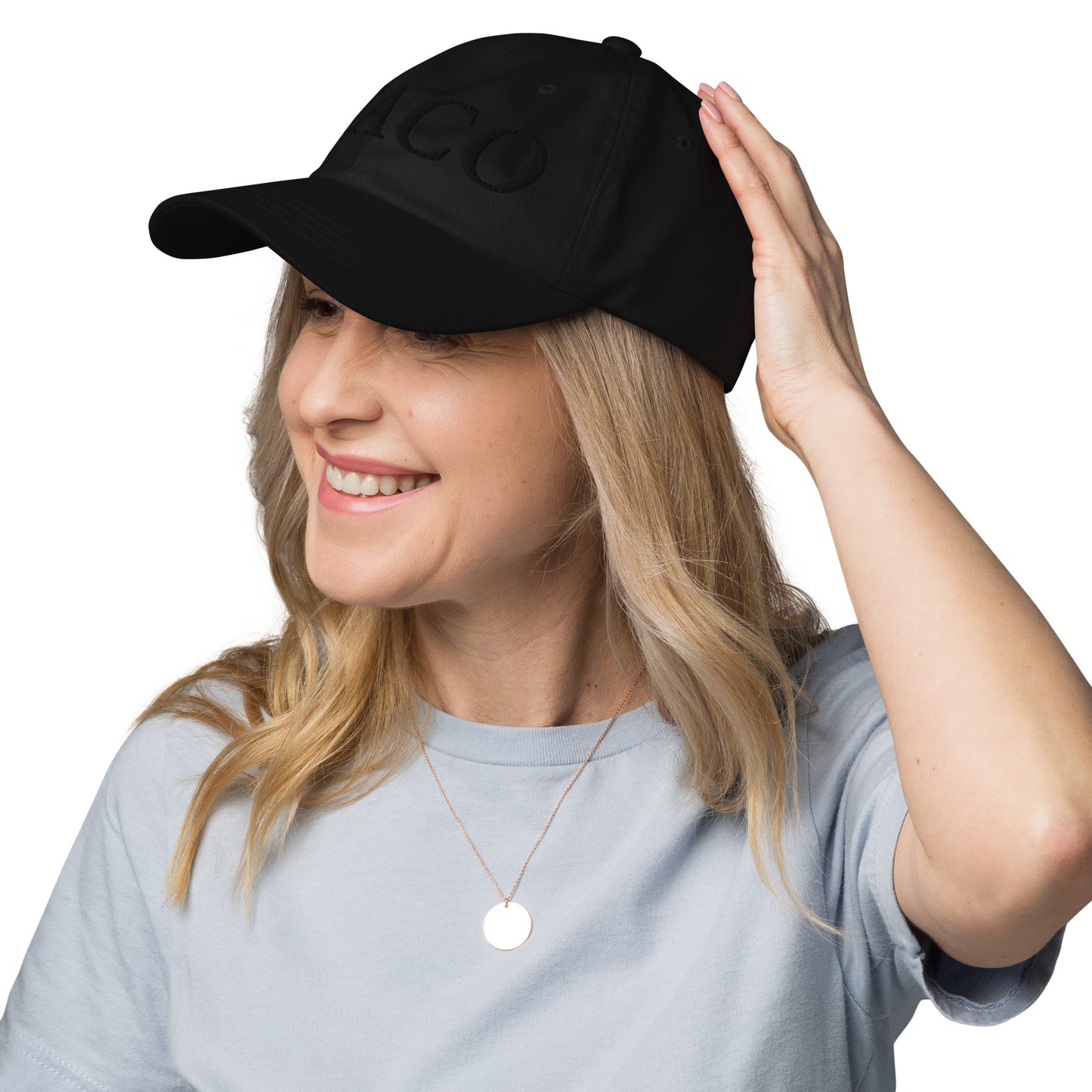 Side profile of black dad hat on blonde model lifting brim, "TACO" embroidery peeking out