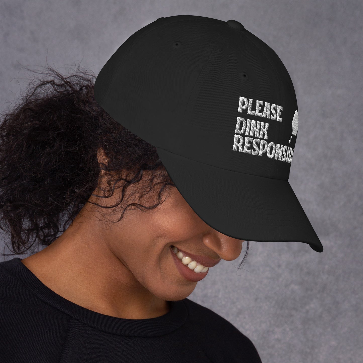 Right 3/4 view of black dad hat on smiling model, "PLEASE DINK RESPONSIBLY" embroidery and pickleball paddle angled