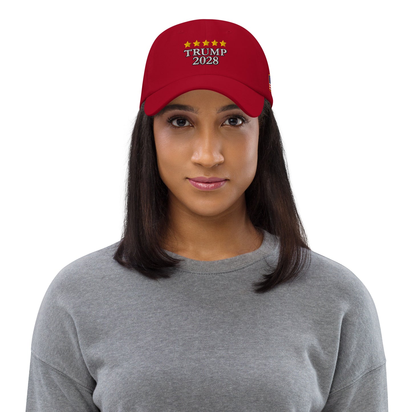 Woman in gray top modeling front of red hat with yellow stars over white "TRUMP 2028" embroidery