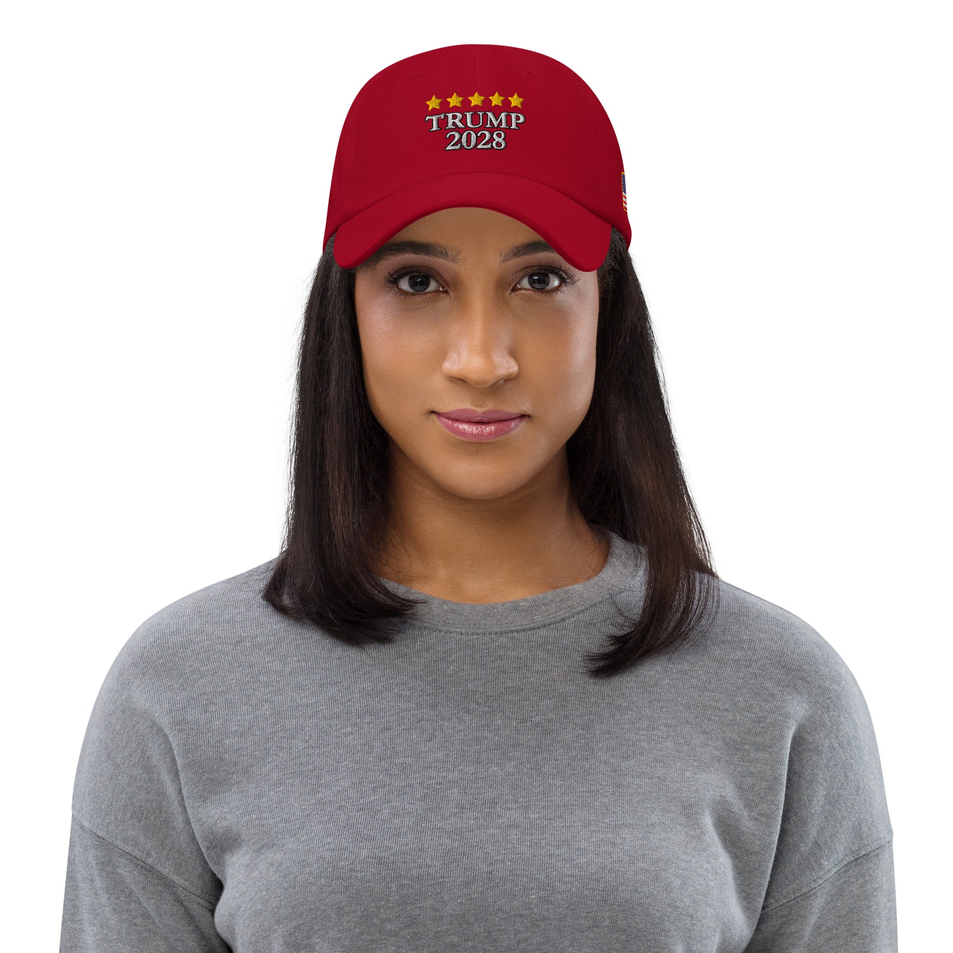 Woman in gray top modeling front of red hat with yellow stars over white "TRUMP 2028" embroidery