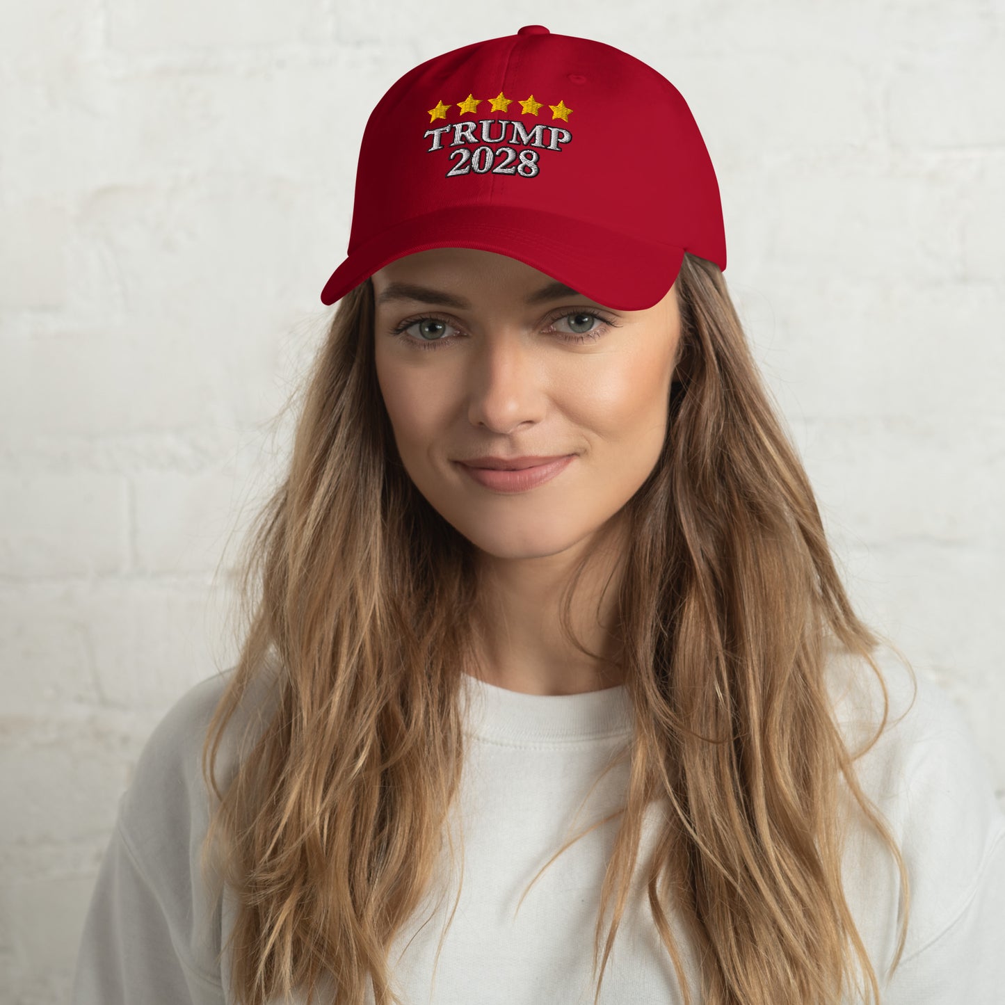 Smiling woman with wavy hair in gray top wearing red "Trump 2028" star-embroidered dad hat