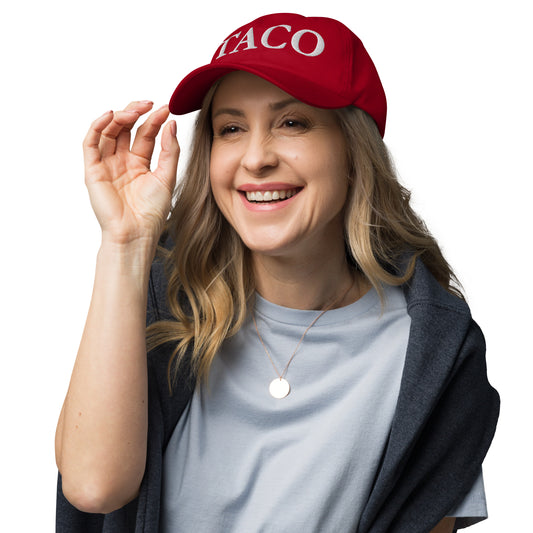 Blonde model playfully tipping brim of red dad hat with white "TACO" embroidery, grinning in gray top