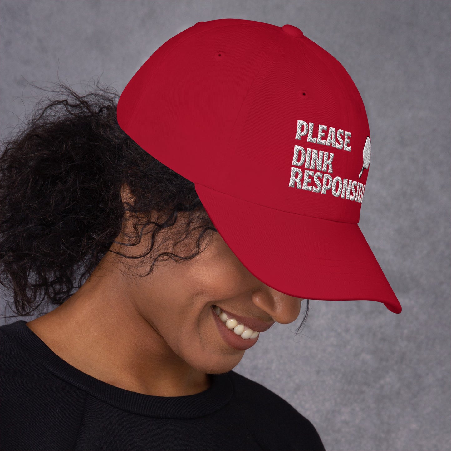 Right 3/4 view of cranberry red dad hat on smiling model, "PLEASE DINK RESPONSIBLY" embroidery and pickleball paddle angled